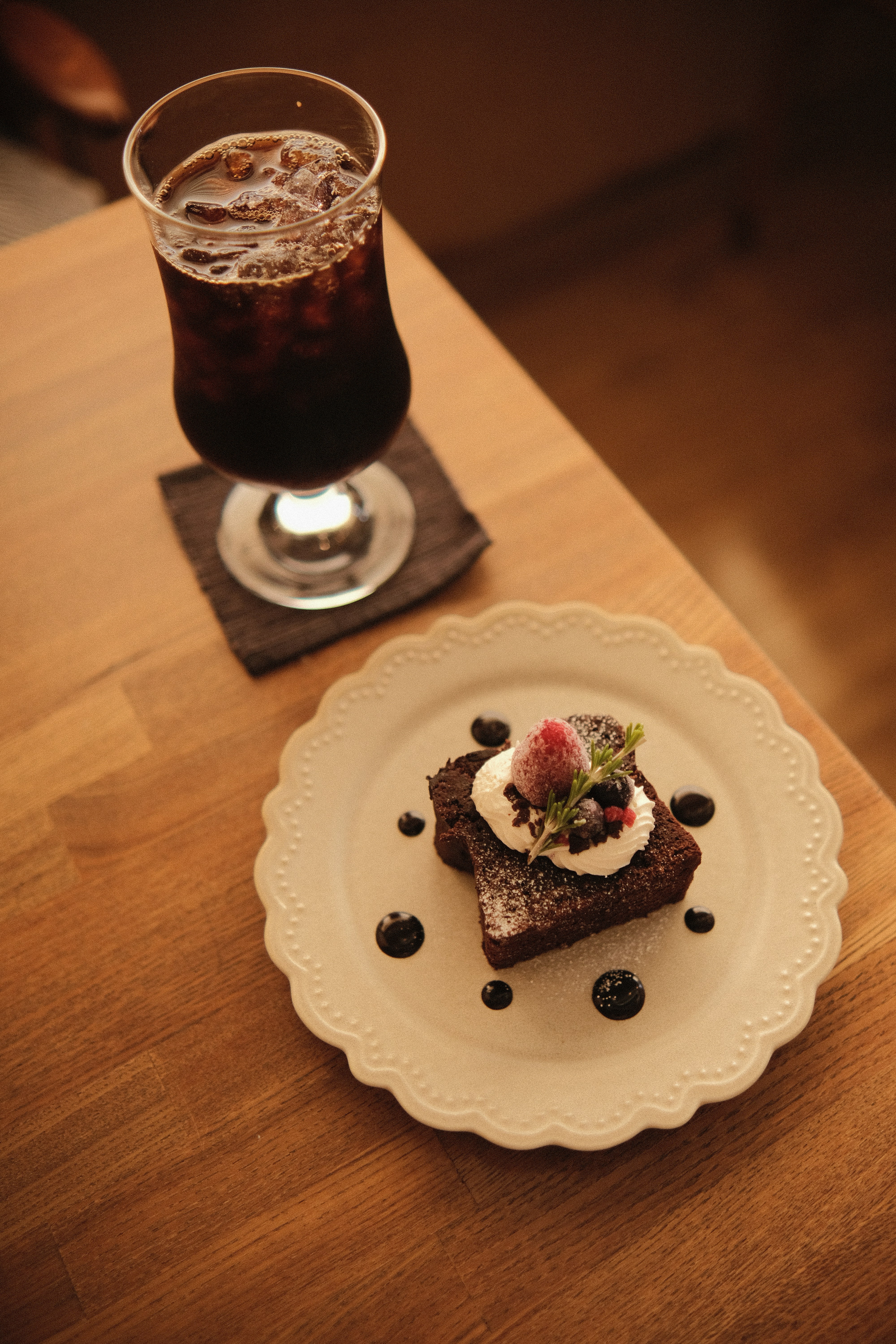 Kue cokelat dengan buah beri dan es kopi di atas meja.