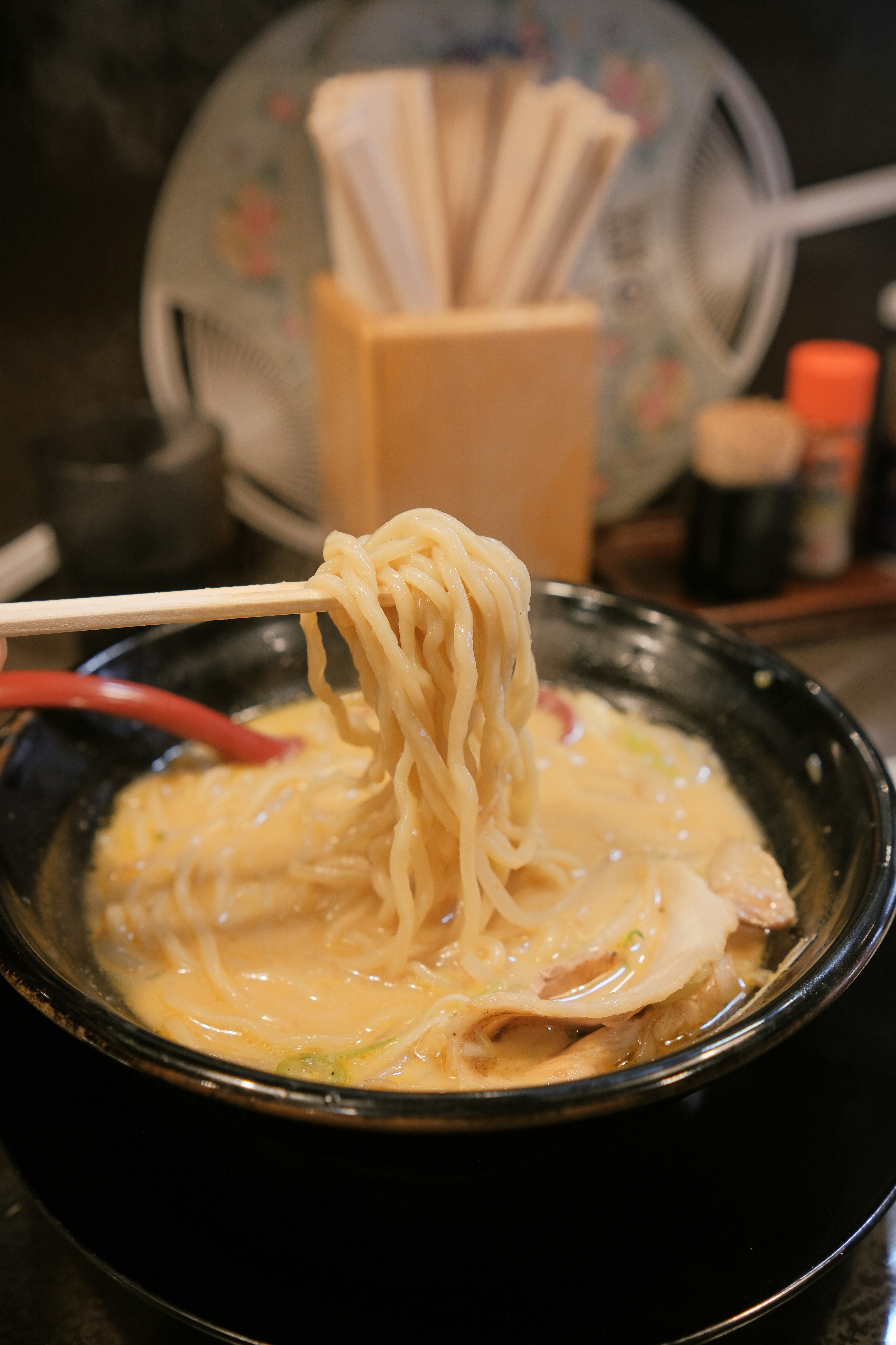 Mie ramen panas diangkat dari sup krim dengan sumpit.