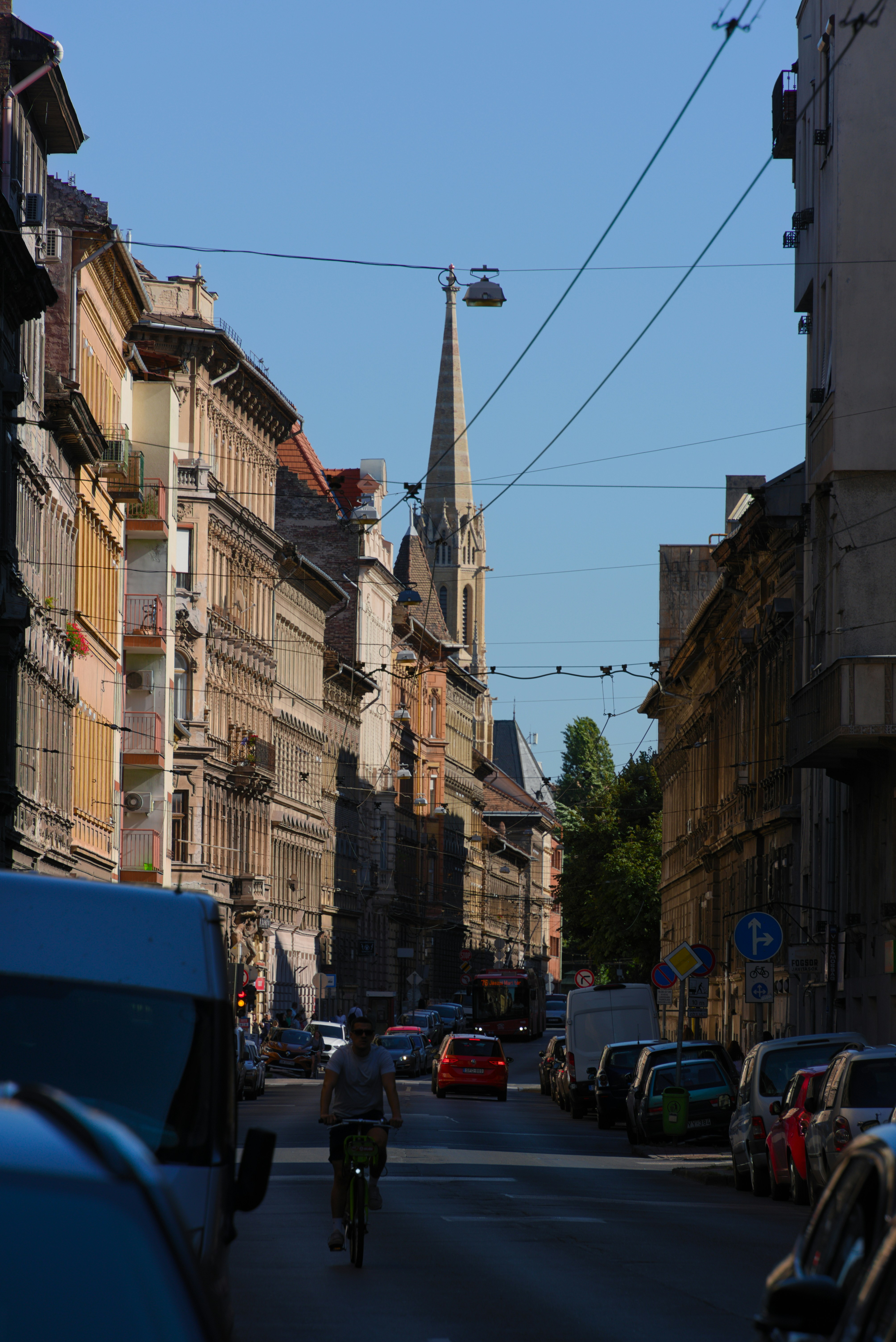 Street with old buildings, cars, a cyclist, and church steeple.