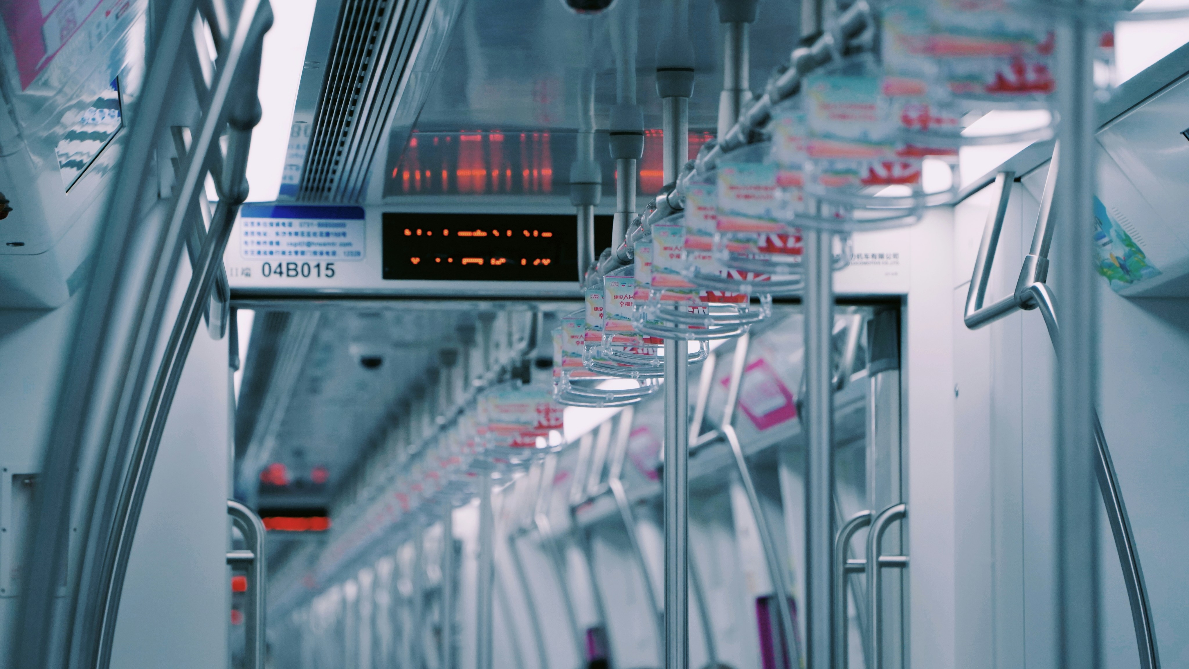 Empty subway train interior with overhead handles and digital display.