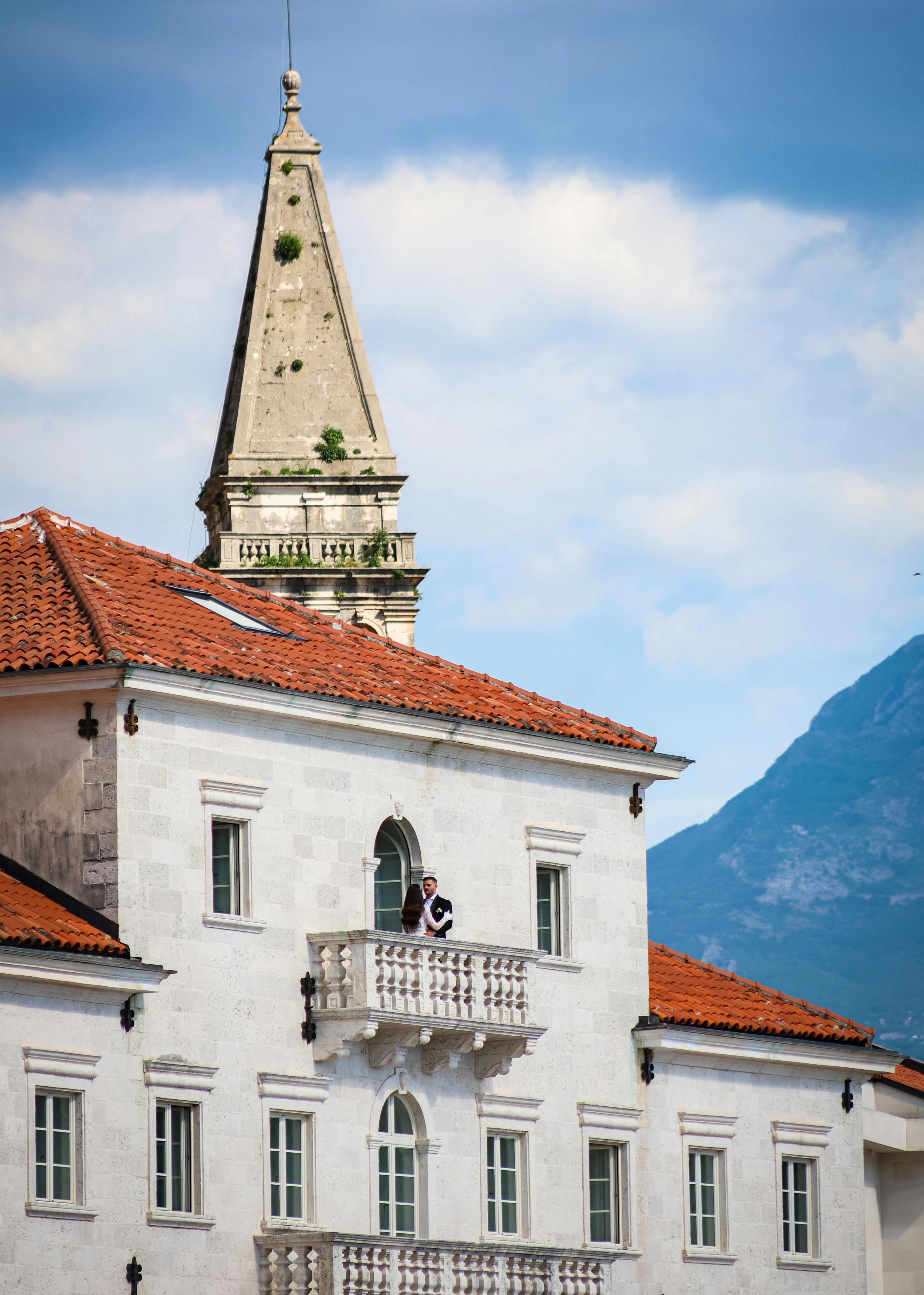 White building with red roof, stone steeple, and mountains.