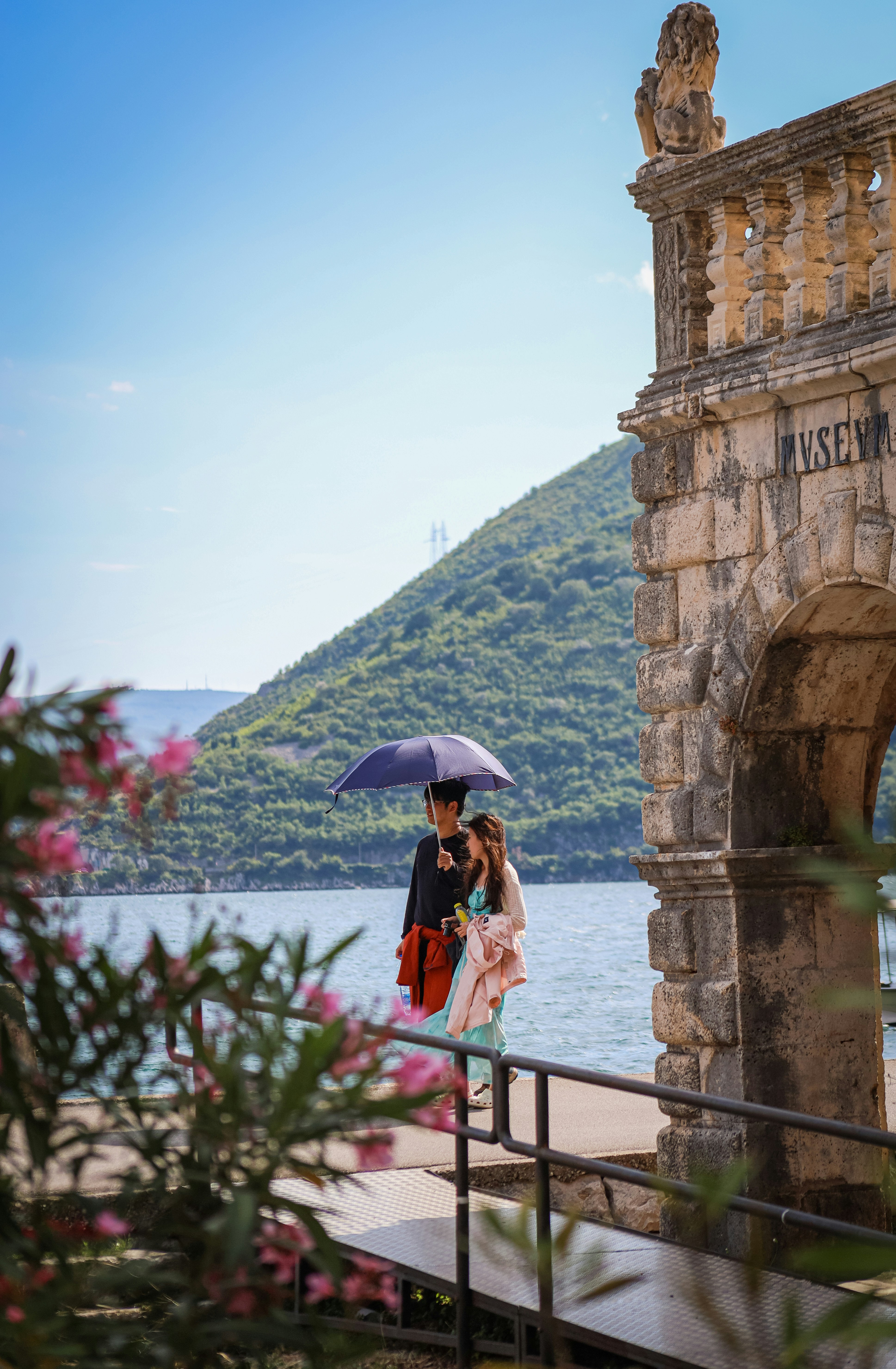 Two people with umbrella walk by a stone archway.