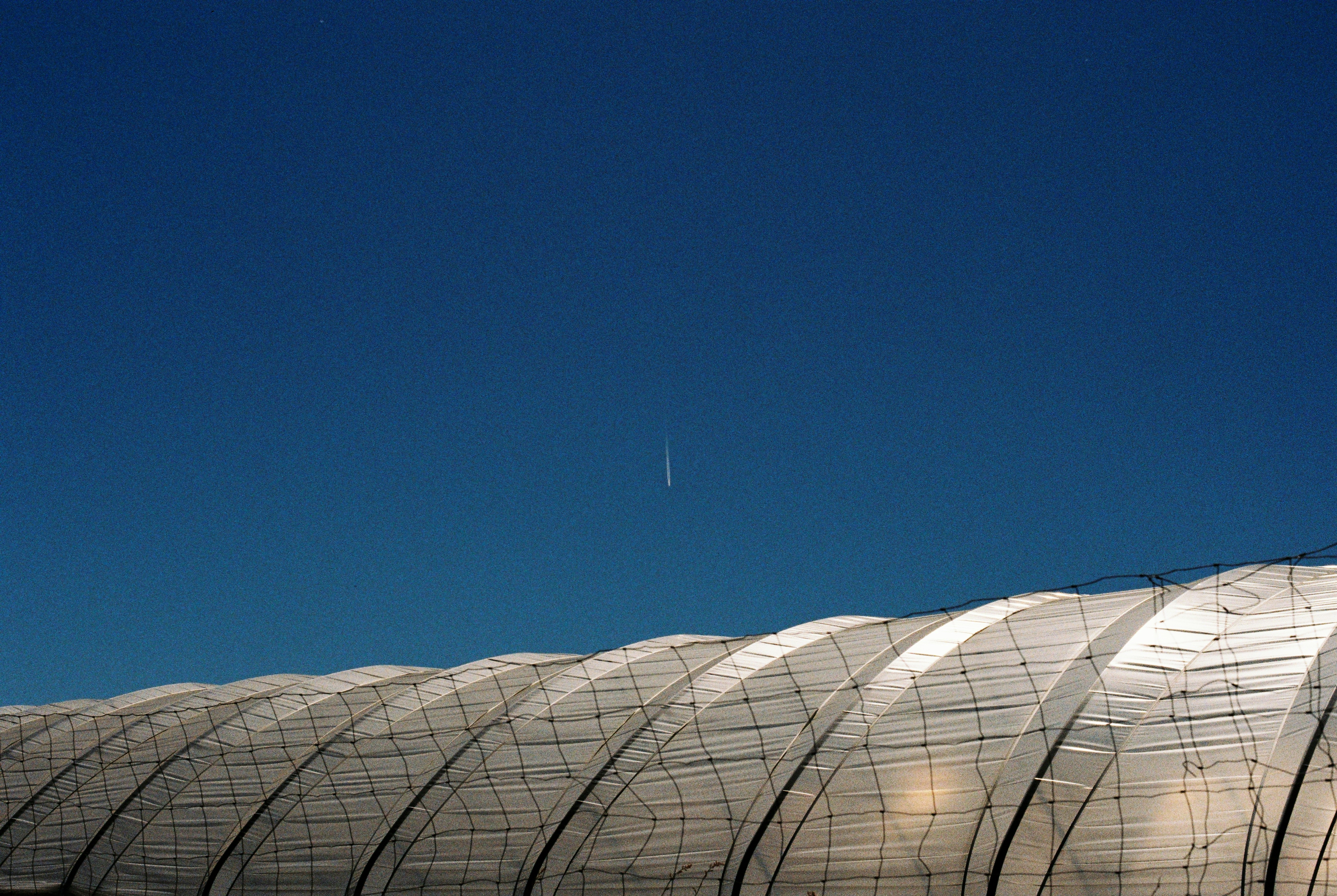 Kondensstreifen im klaren blauen Himmel über einem geschwungenen architektonischen Dach.