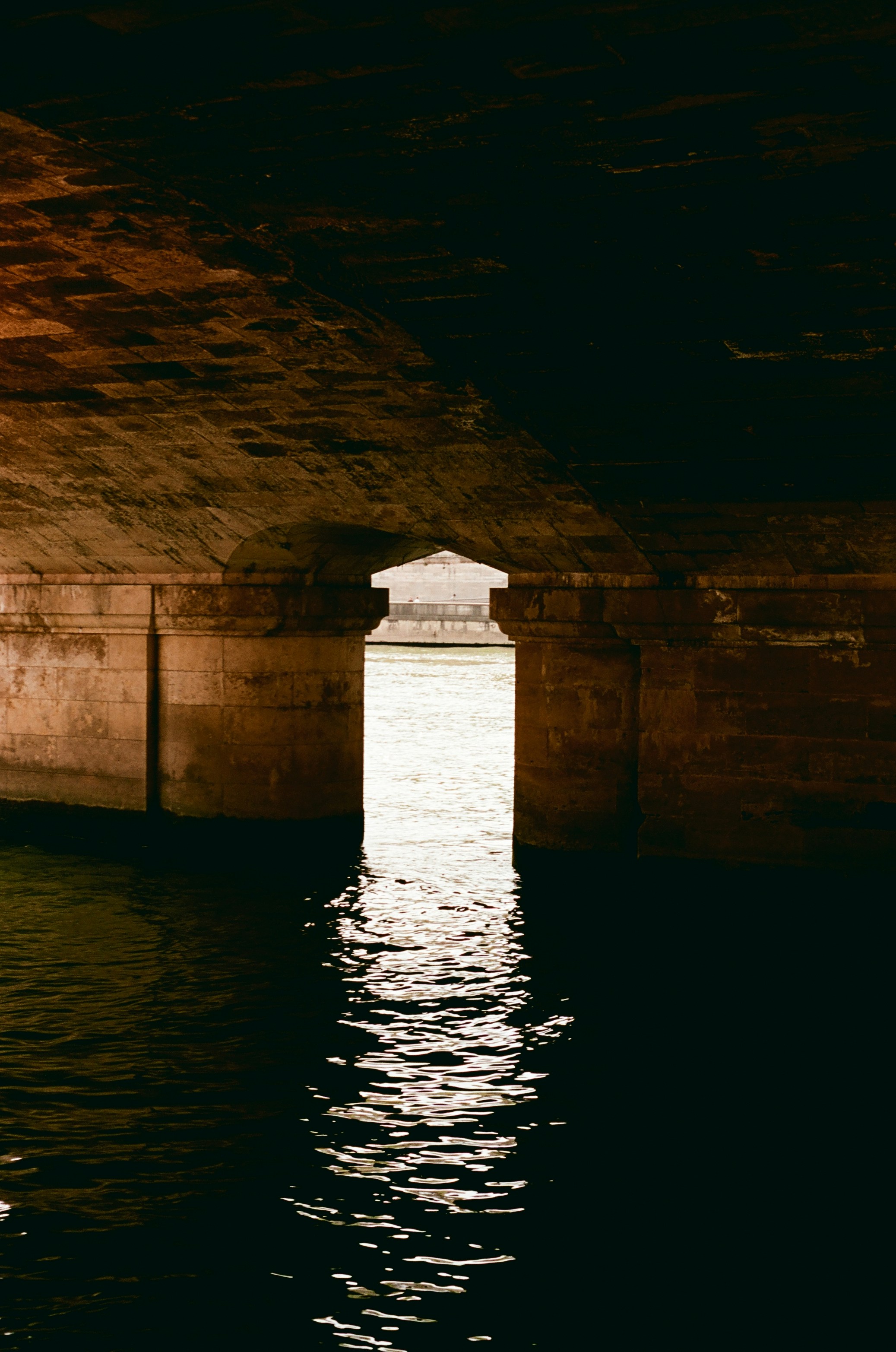 Light shines through a dark archway onto rippling water.