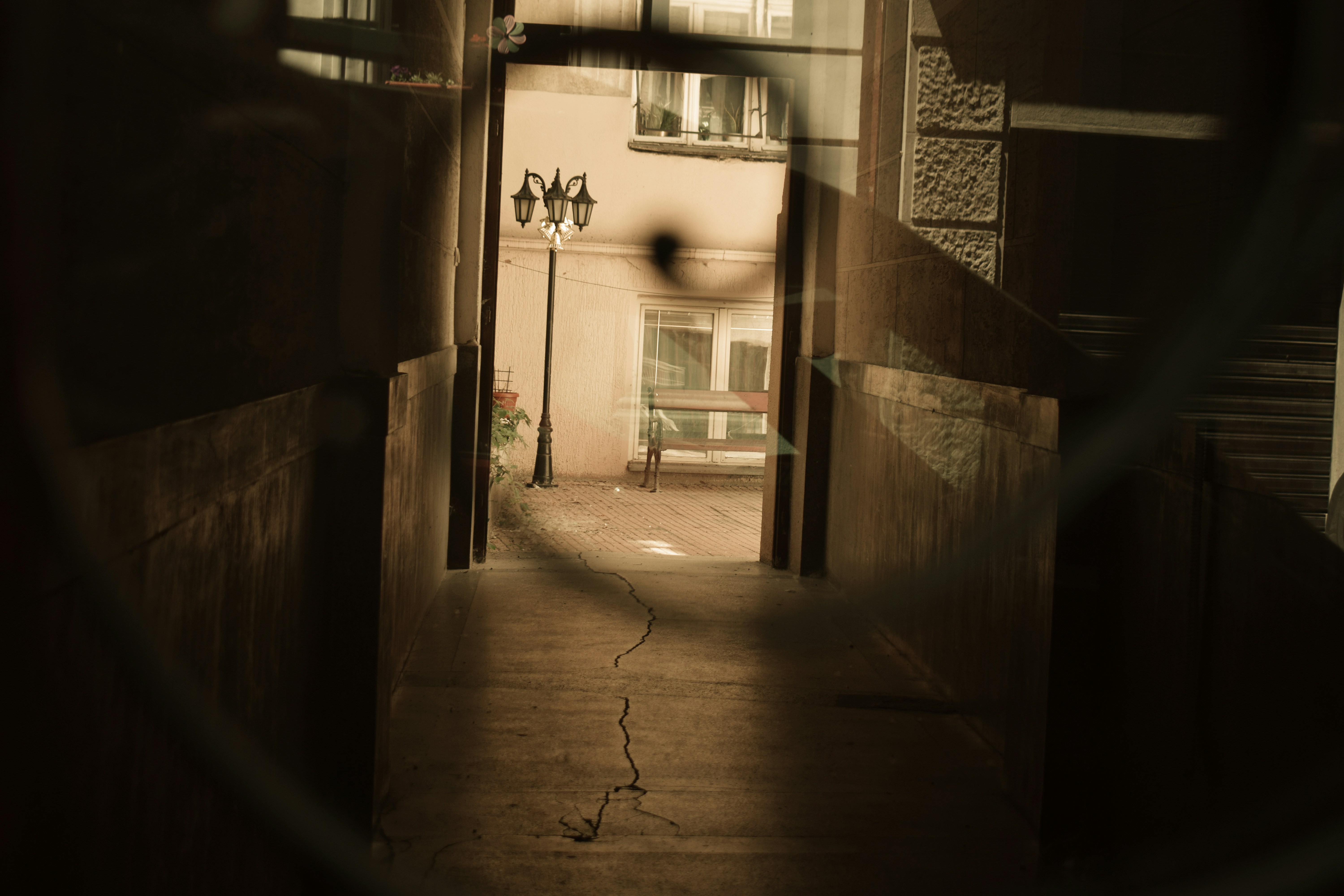 Dark passage opens to a bright courtyard with a streetlamp.