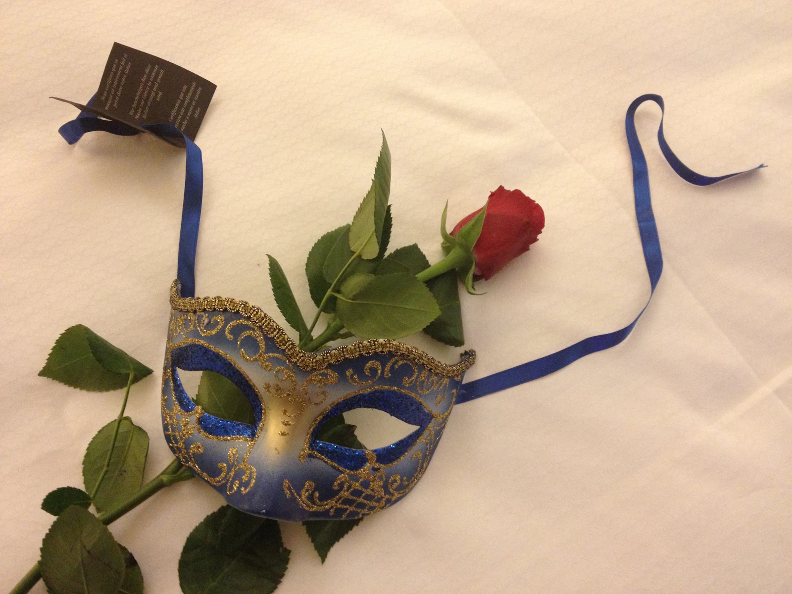 Venezianische Maske und rote Rose auf weißem Laken