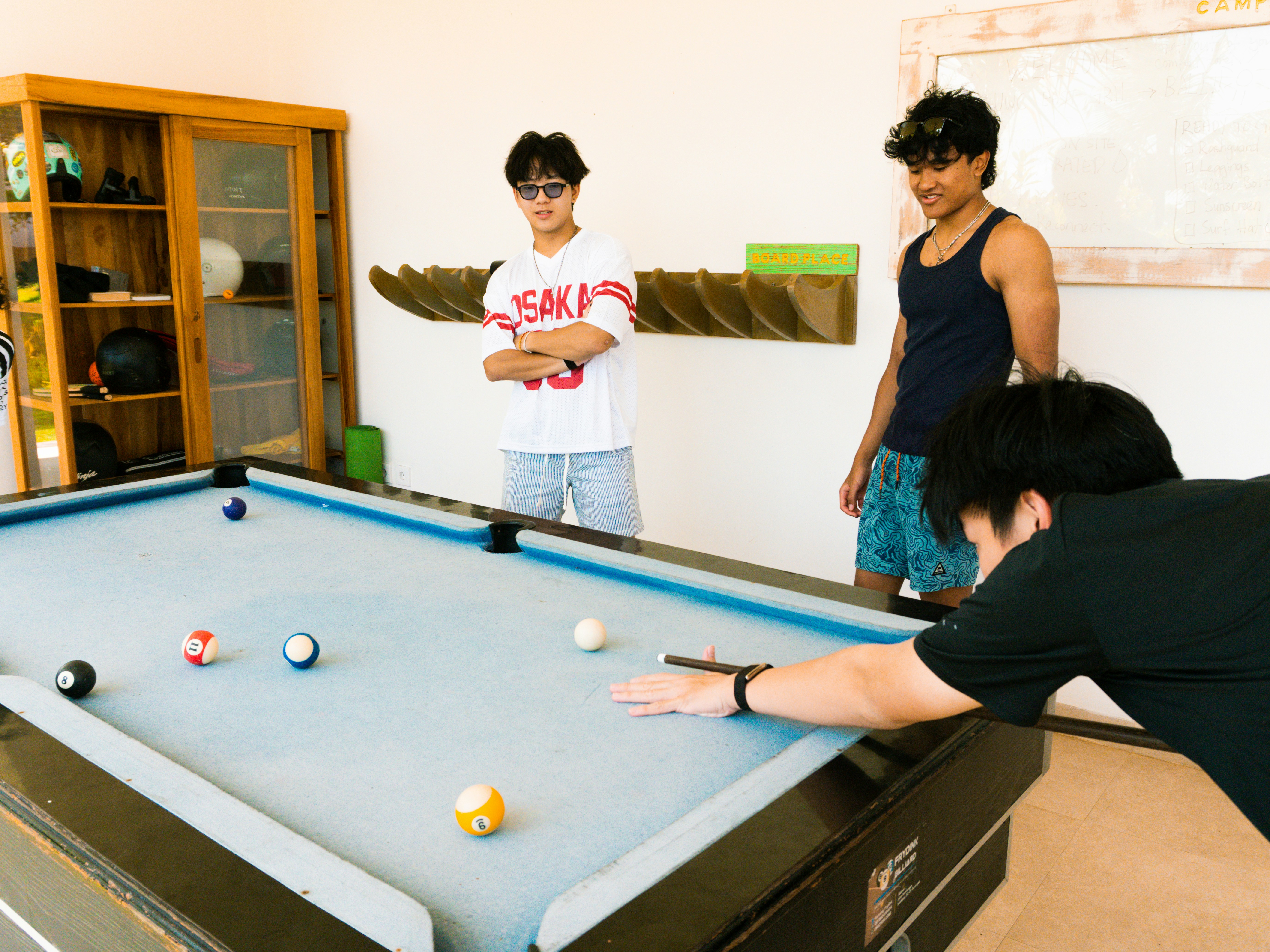 Young men playing billiards on a light blue pool table.