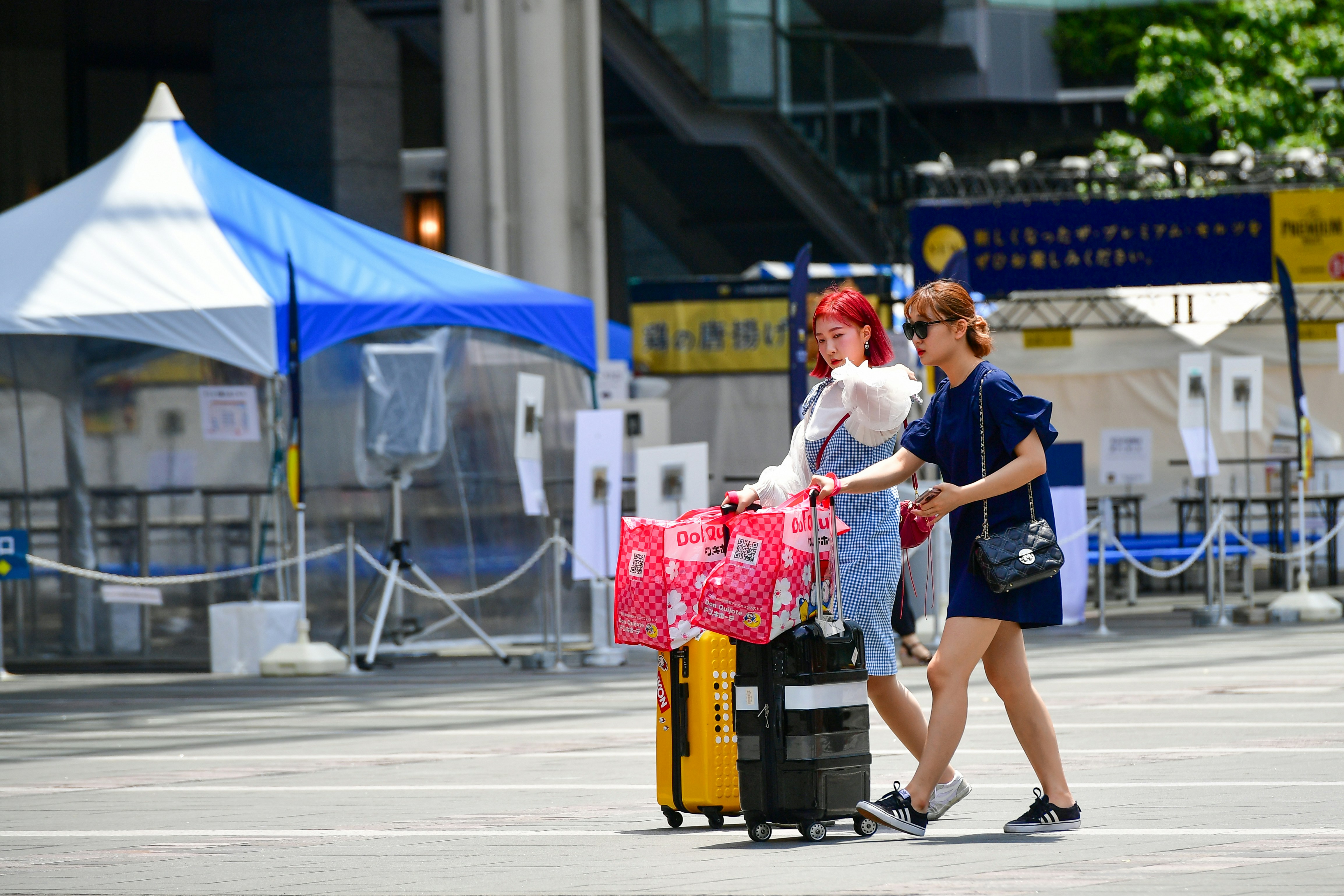 Two stylish young Asian women walking across an open city square with heavy luggage, suitcases, and shopping bags during