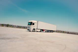 A white semi-truck parked on concrete under a blue sky.
