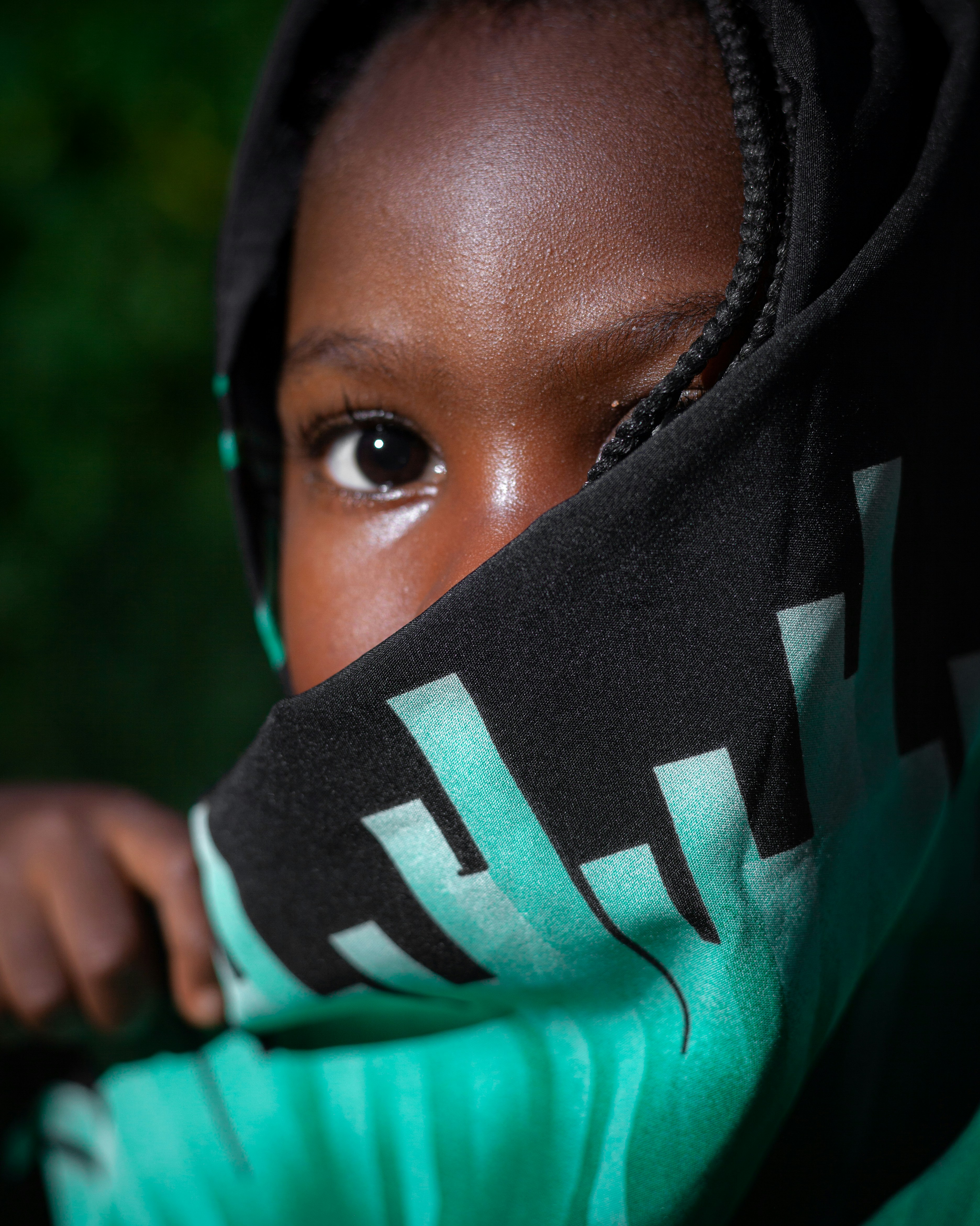 Ojo de niño asomando por una sudadera verde y negra.