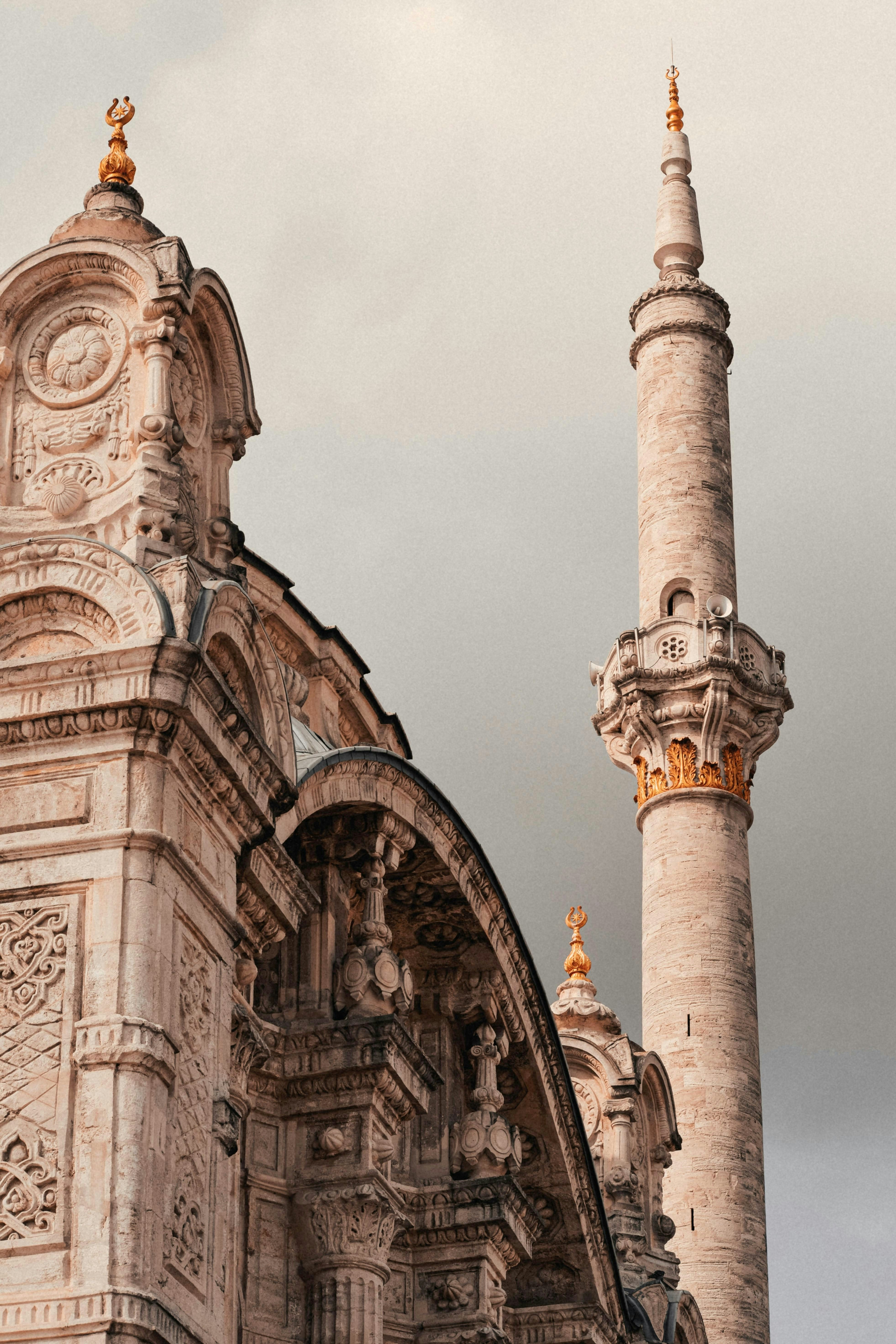 Ornate mosque architecture with a tall minaret against cloudy sky