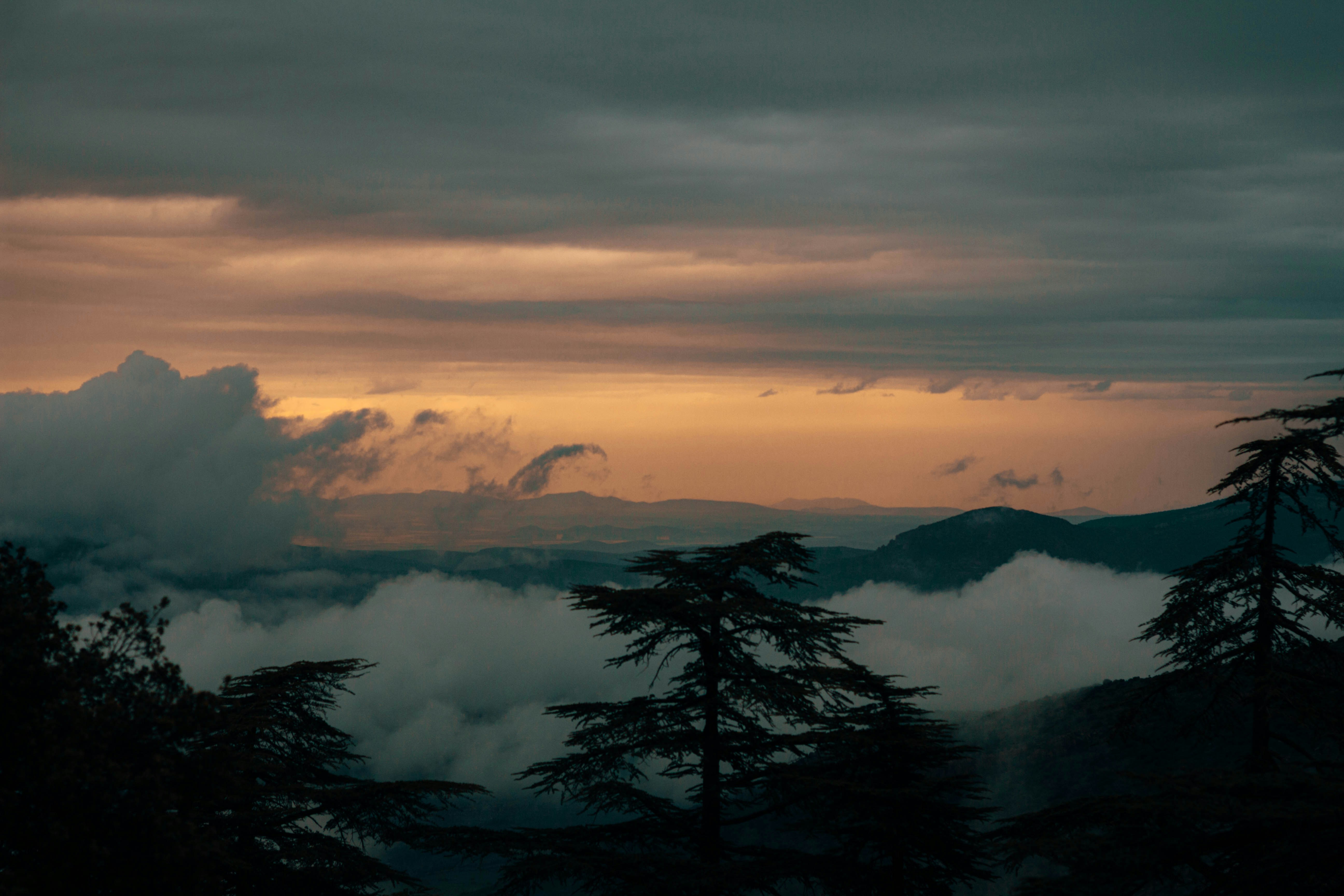 Paisagem montanhosa escura com nuvens e um céu vibrante ao pôr do sol.