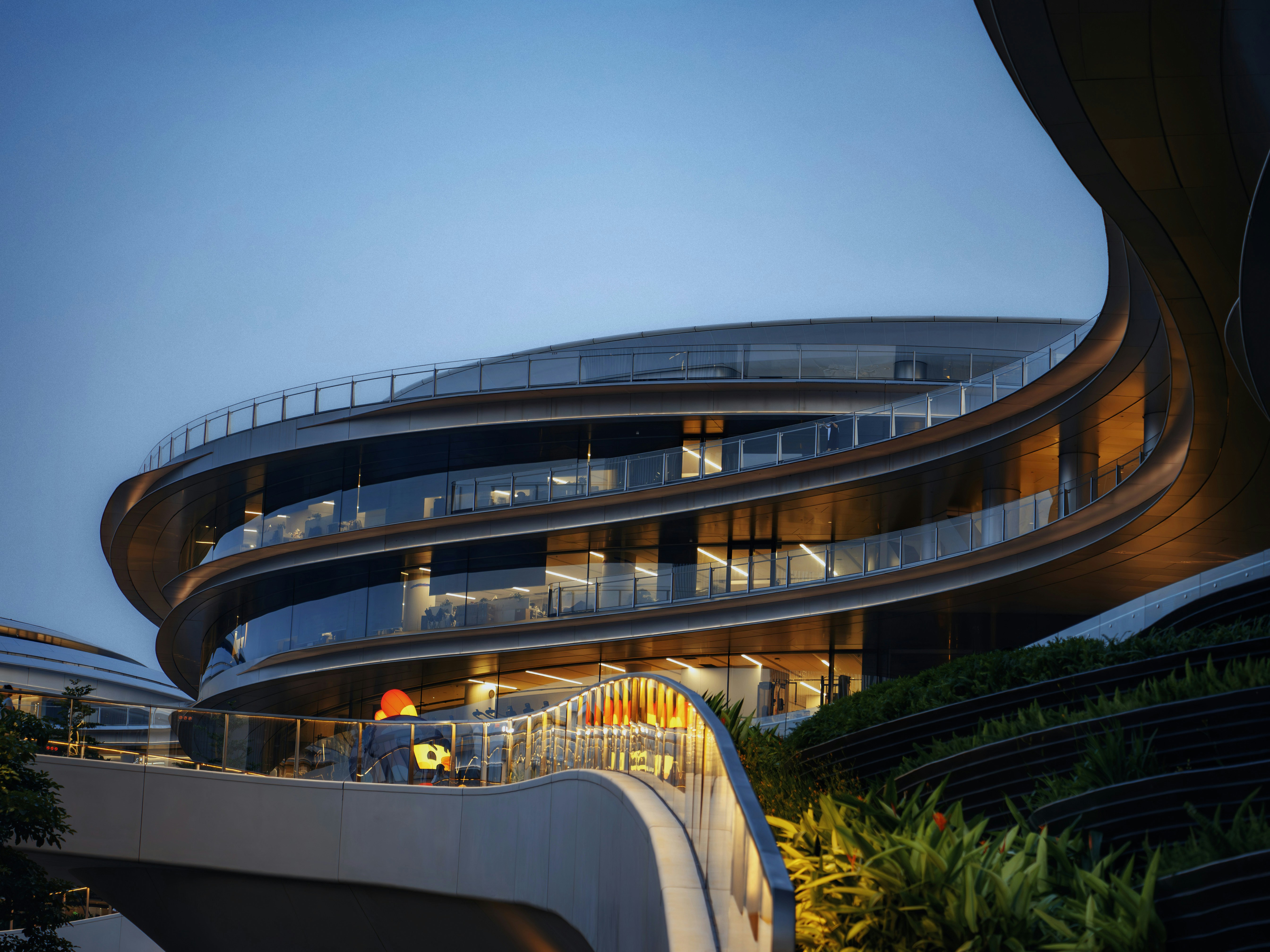 Contemporary curved building illuminated at twilight with lush landscaping.