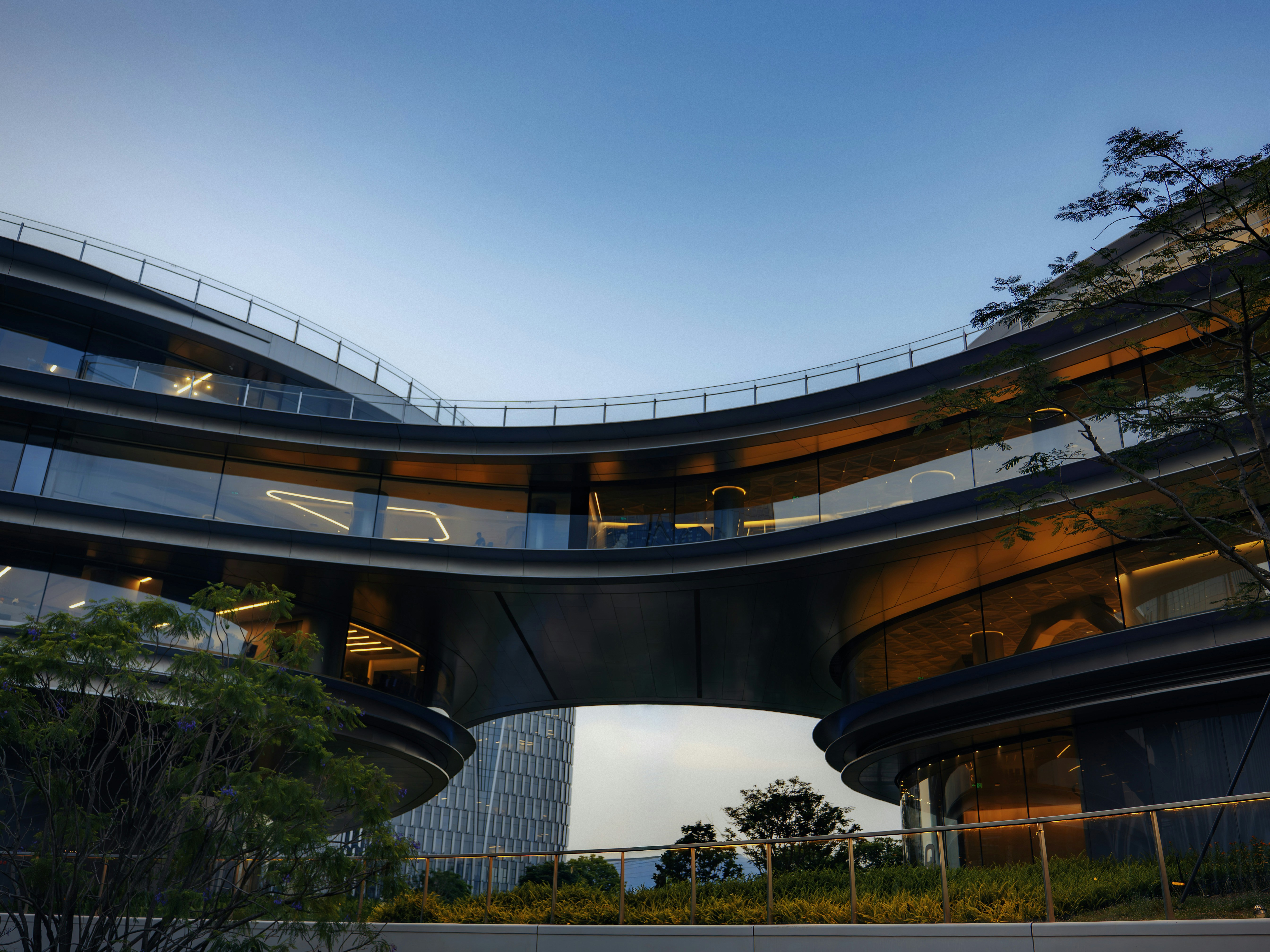 Modern curved building with green terraces under a clear sky.