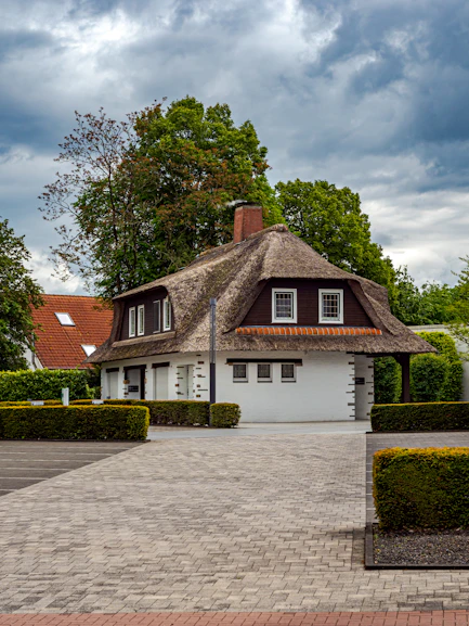 A white house with a thatched roof and paved driveway.
