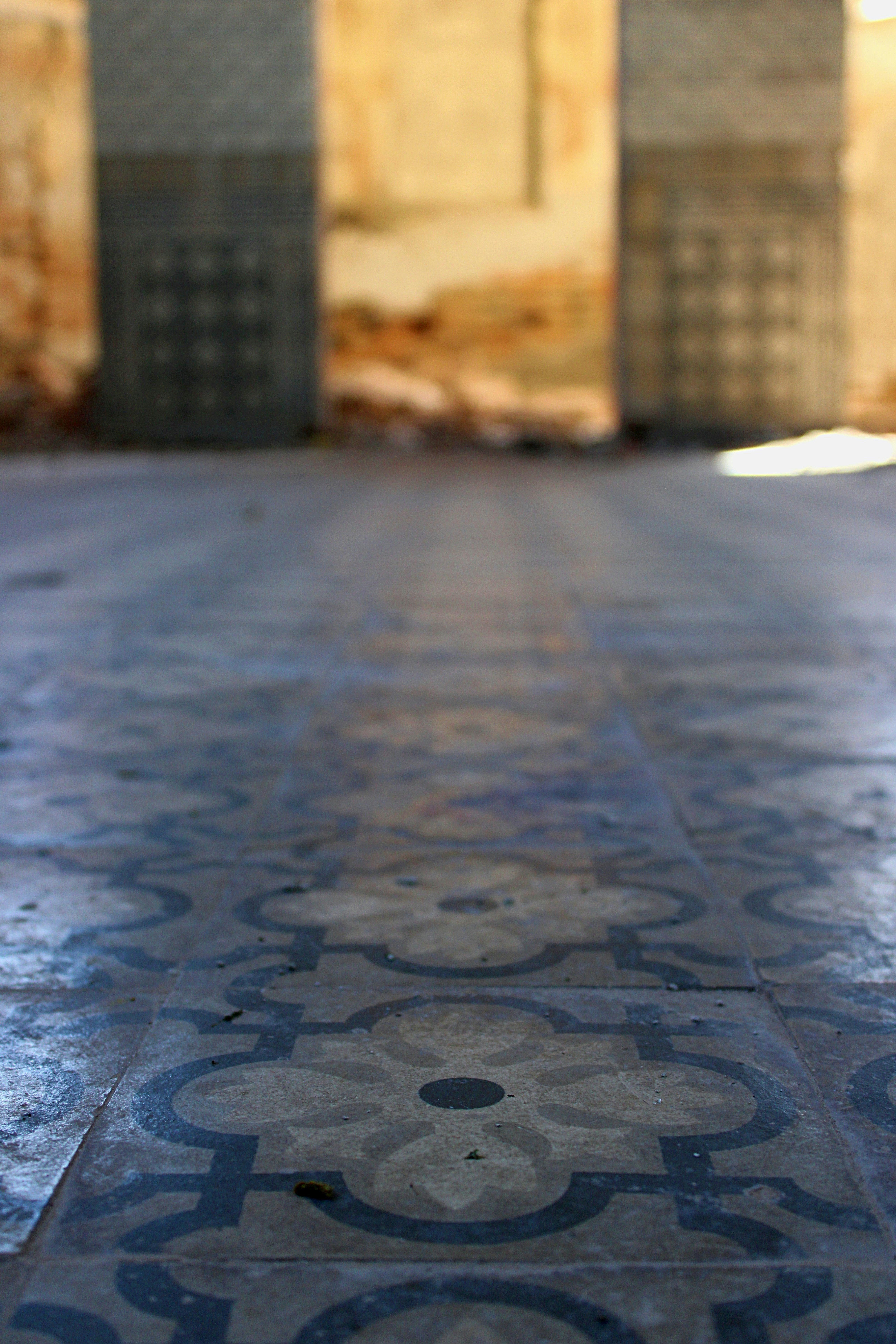 Patterned floor tiles lead to blurred pillars and a wall.