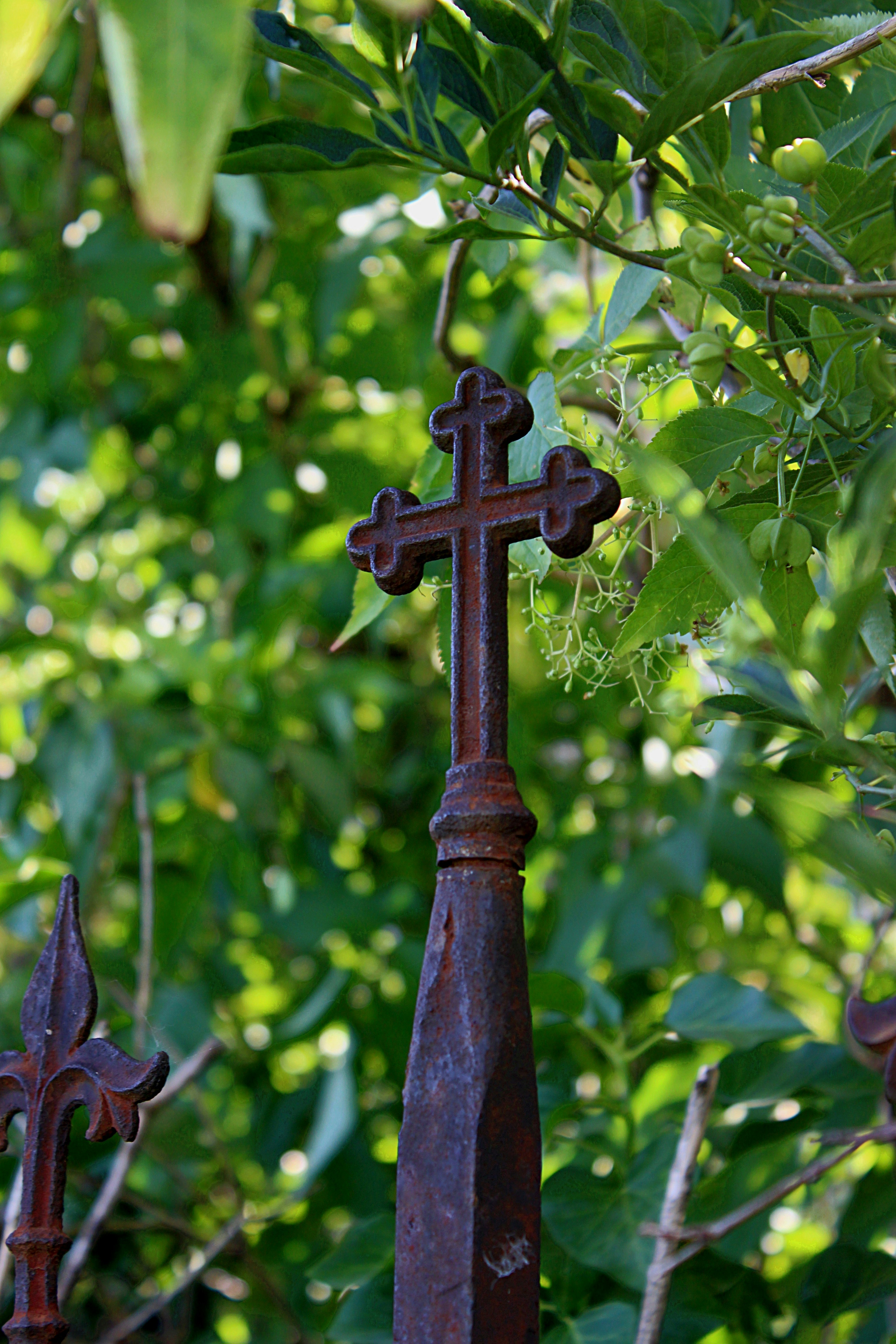 Rusty metal cross on a fence post.