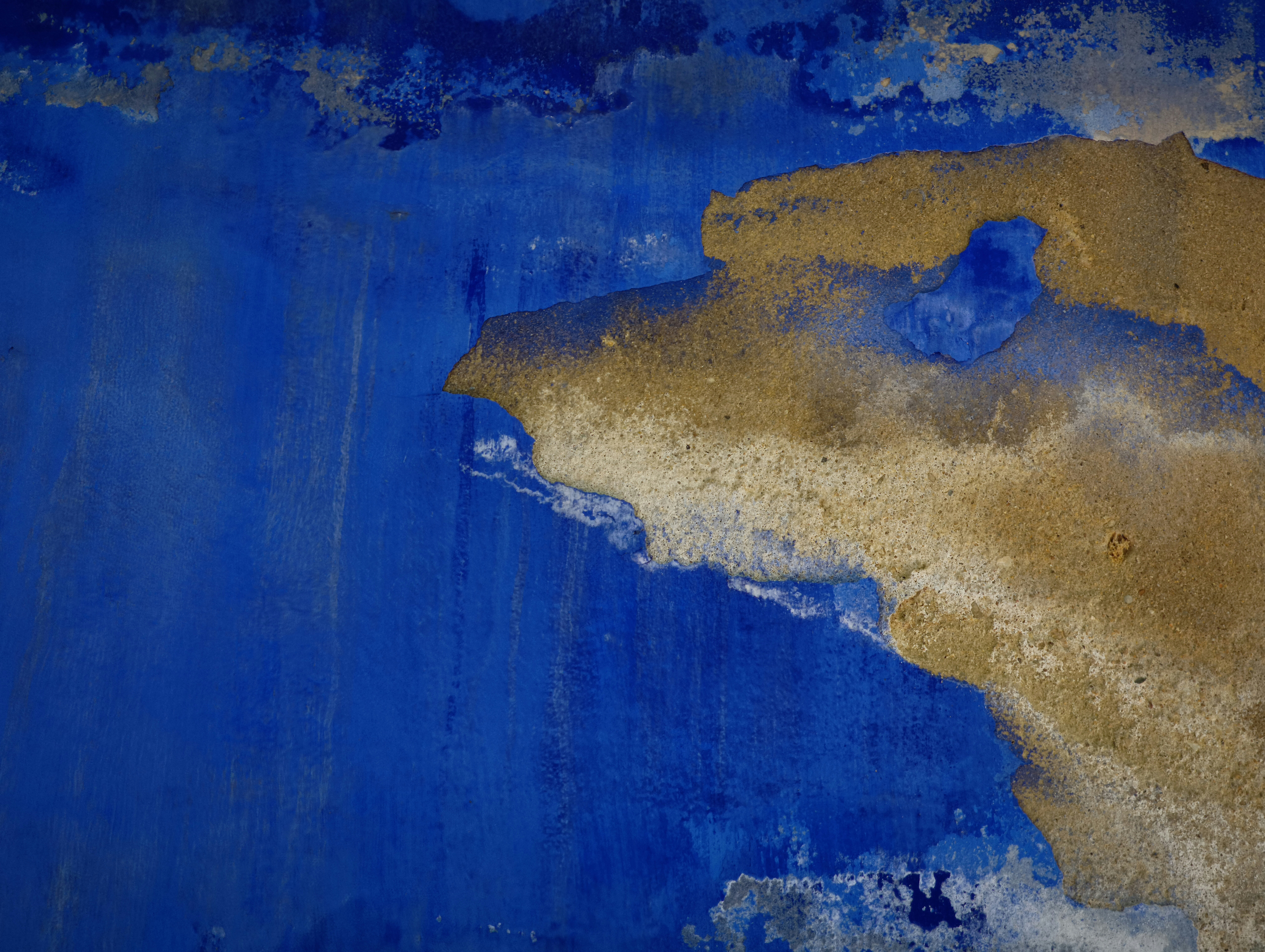 Abblätternde blaue Farbe offenbart eine strukturierte braune Oberfläche darunter.