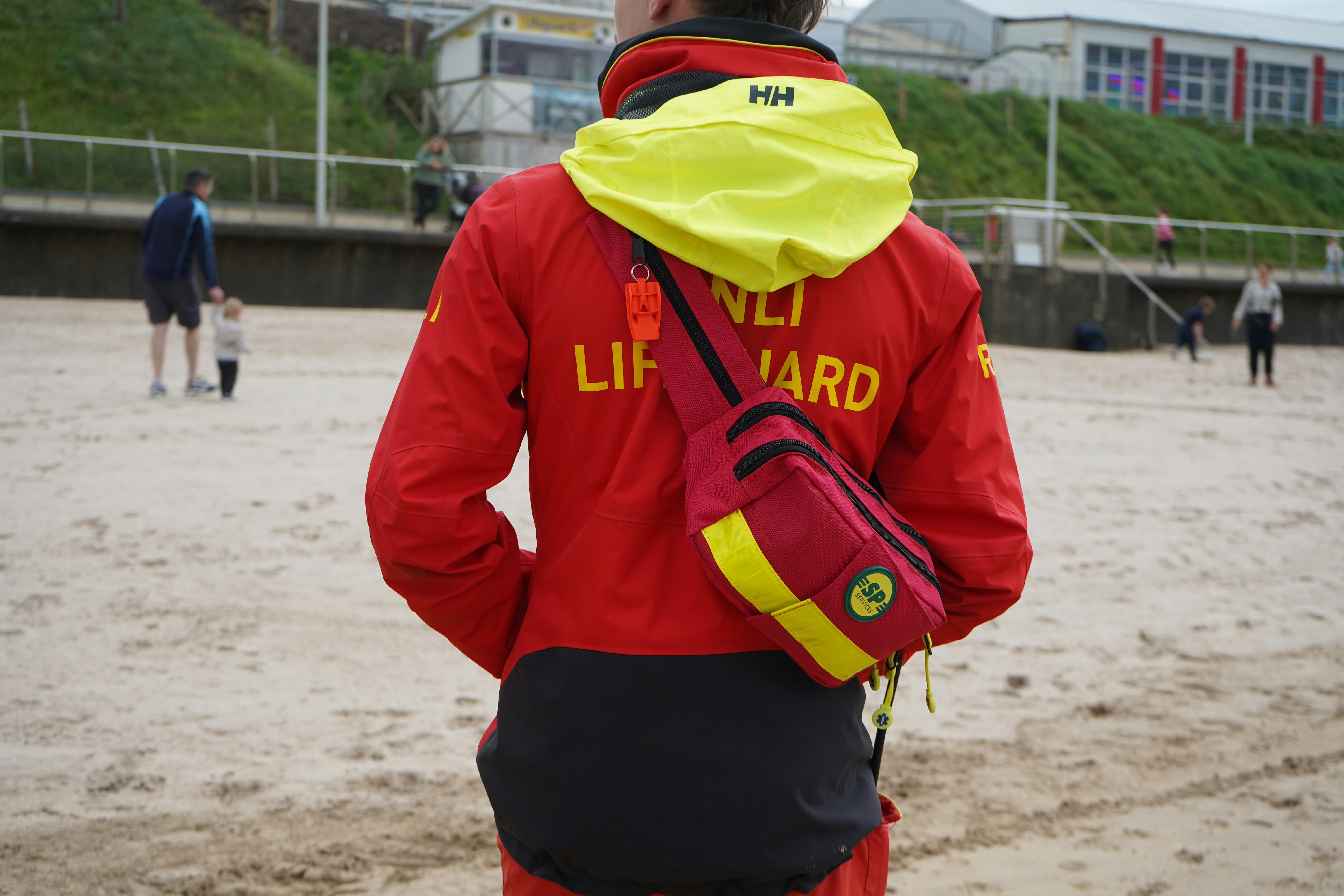 Rnli lifeguard in red jacket on a sandy beach.