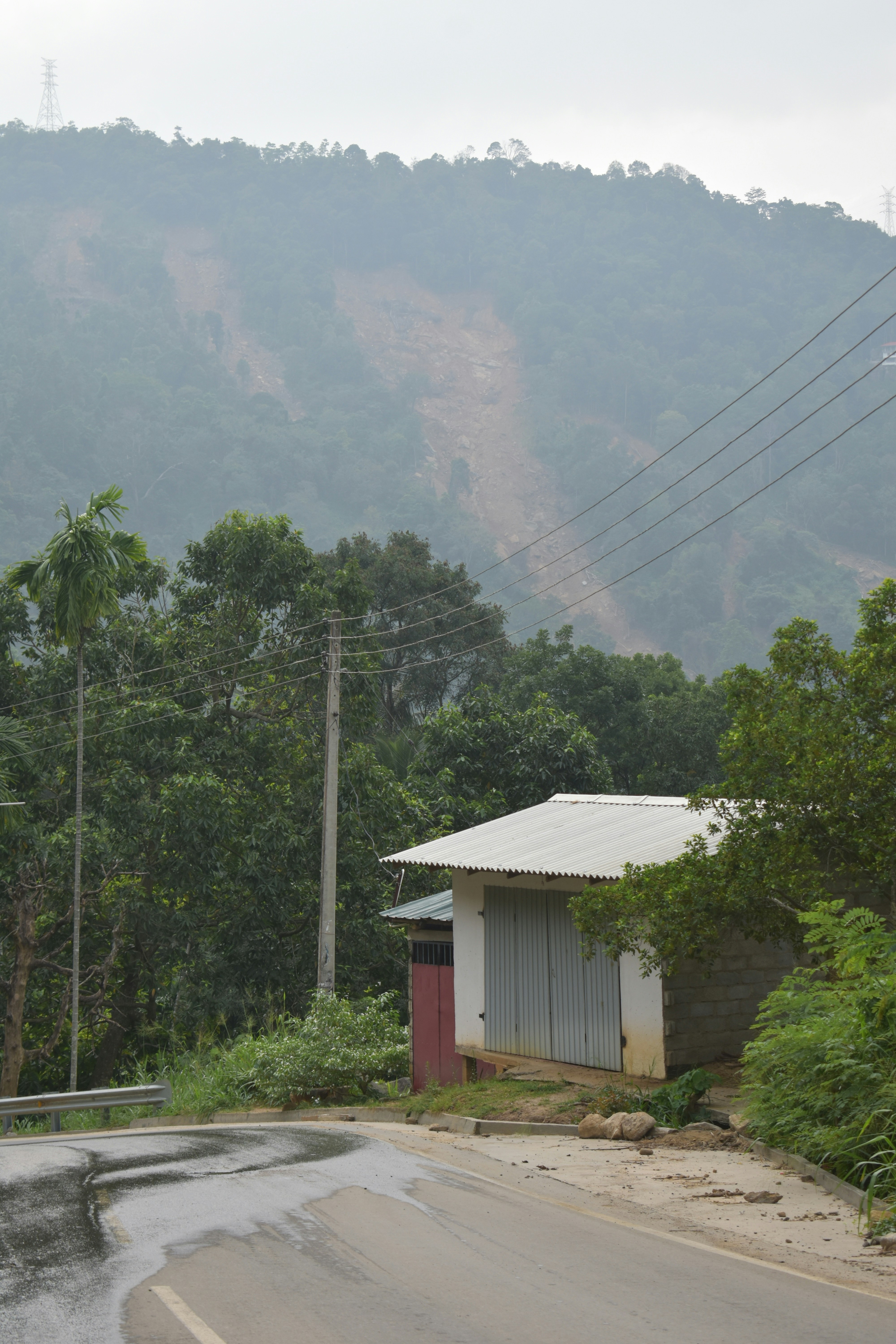 Building by wet road, power lines, and distant mountain landslide.