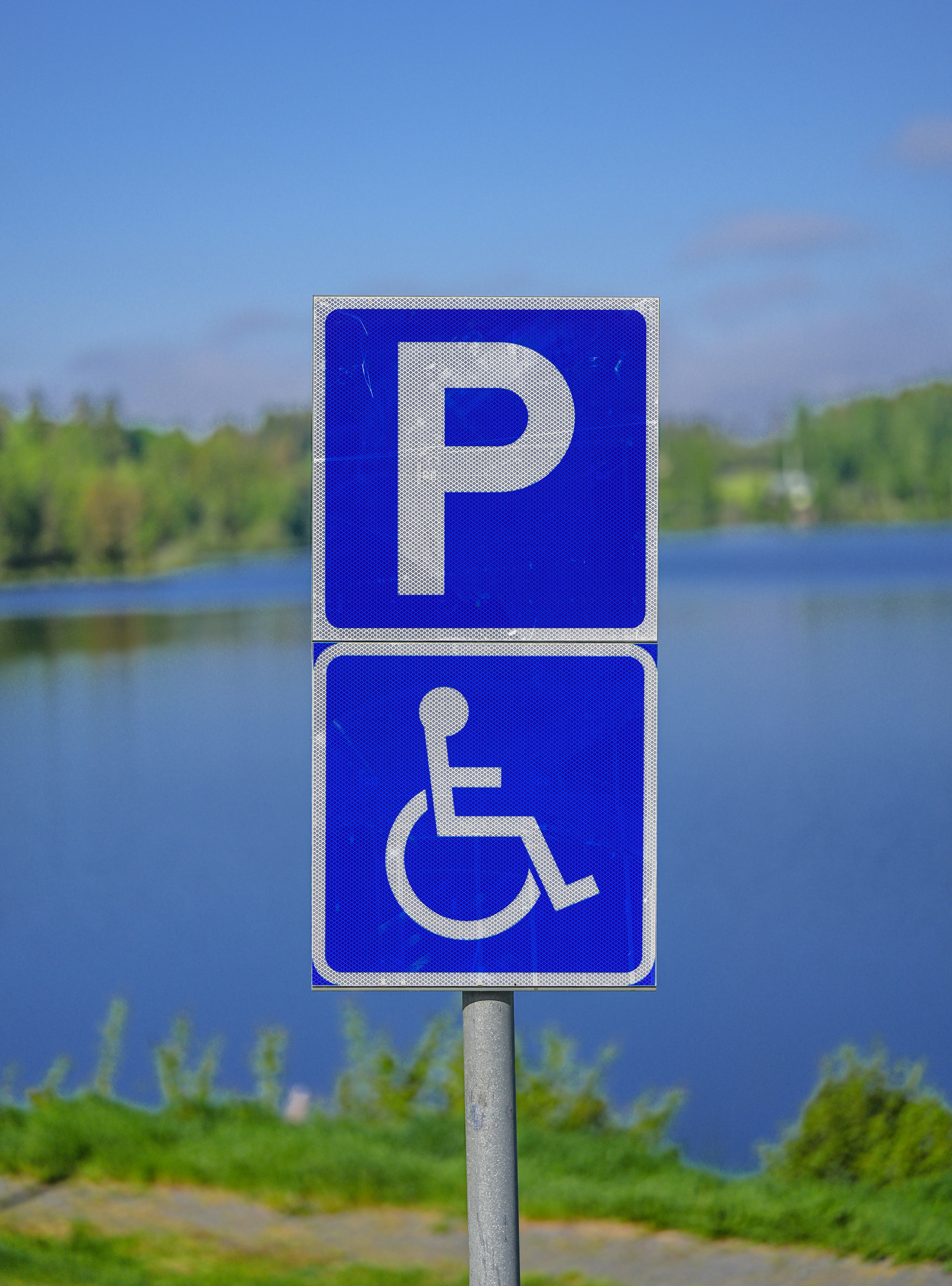 Tanda parkir penyandang disabilitas biru berdiri di tepi danau.