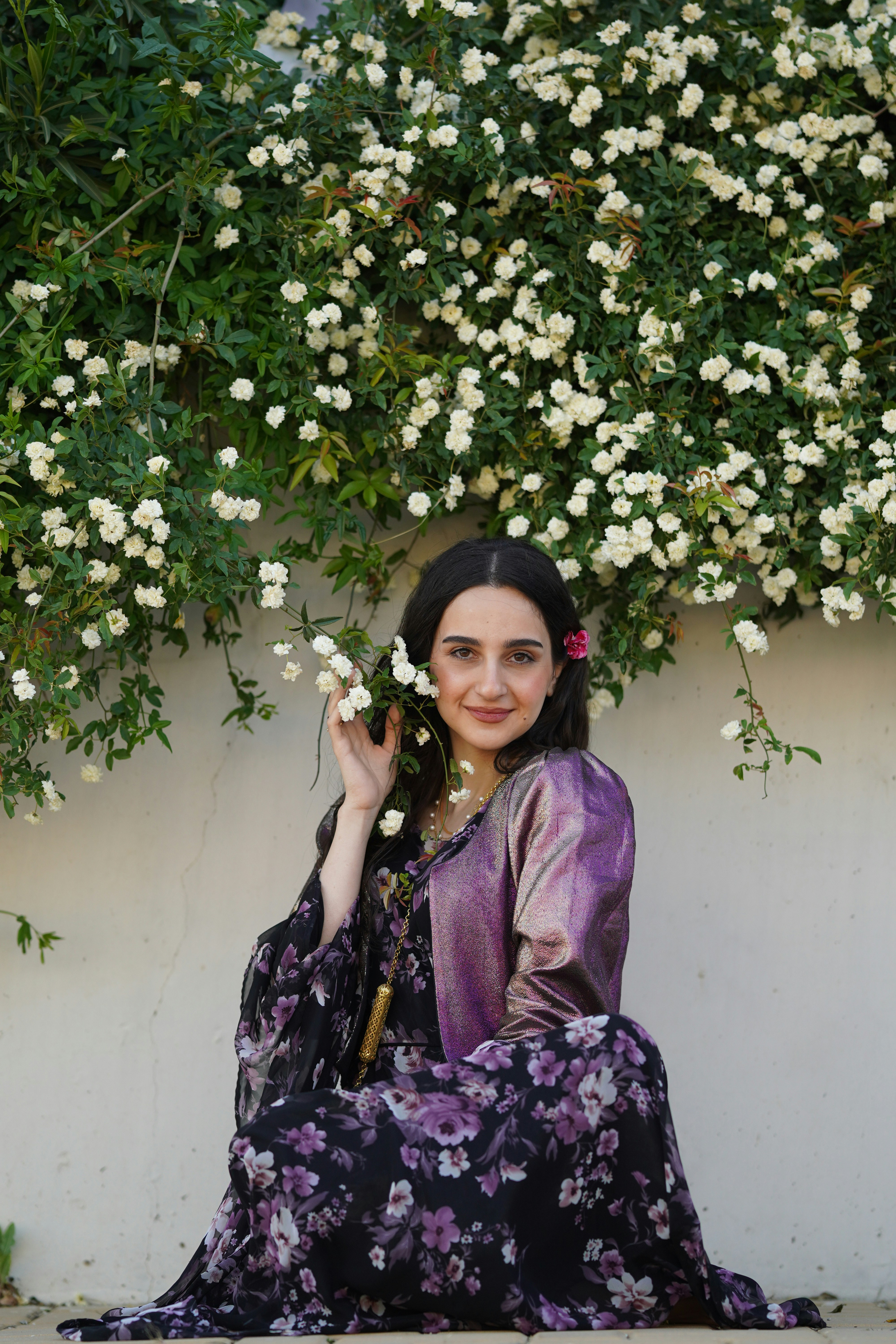 Mujer sonriente con un vestido floral y rosas trepadoras blancas.