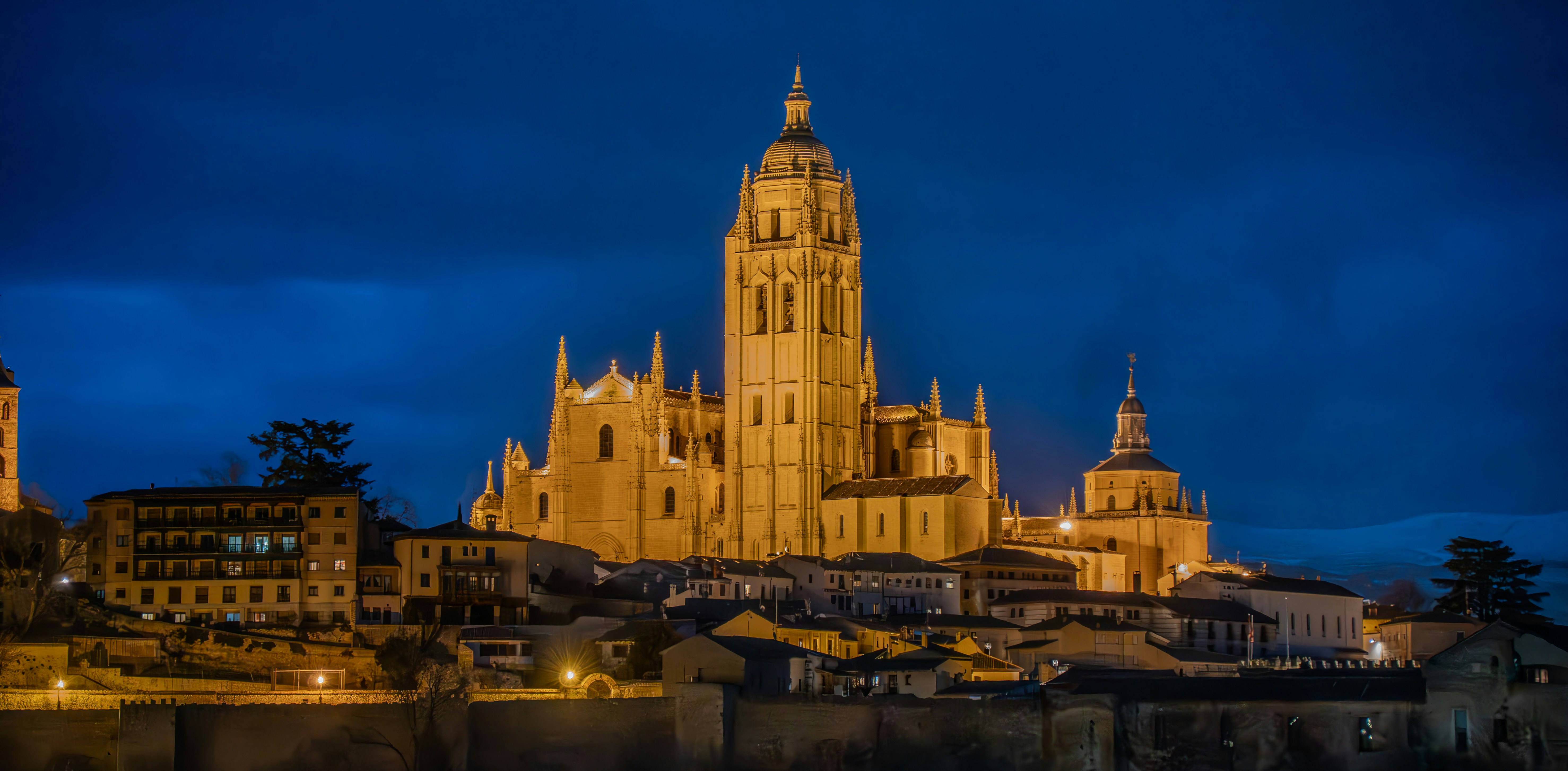 A grand illuminated cathedral overlooks a historic city at night.