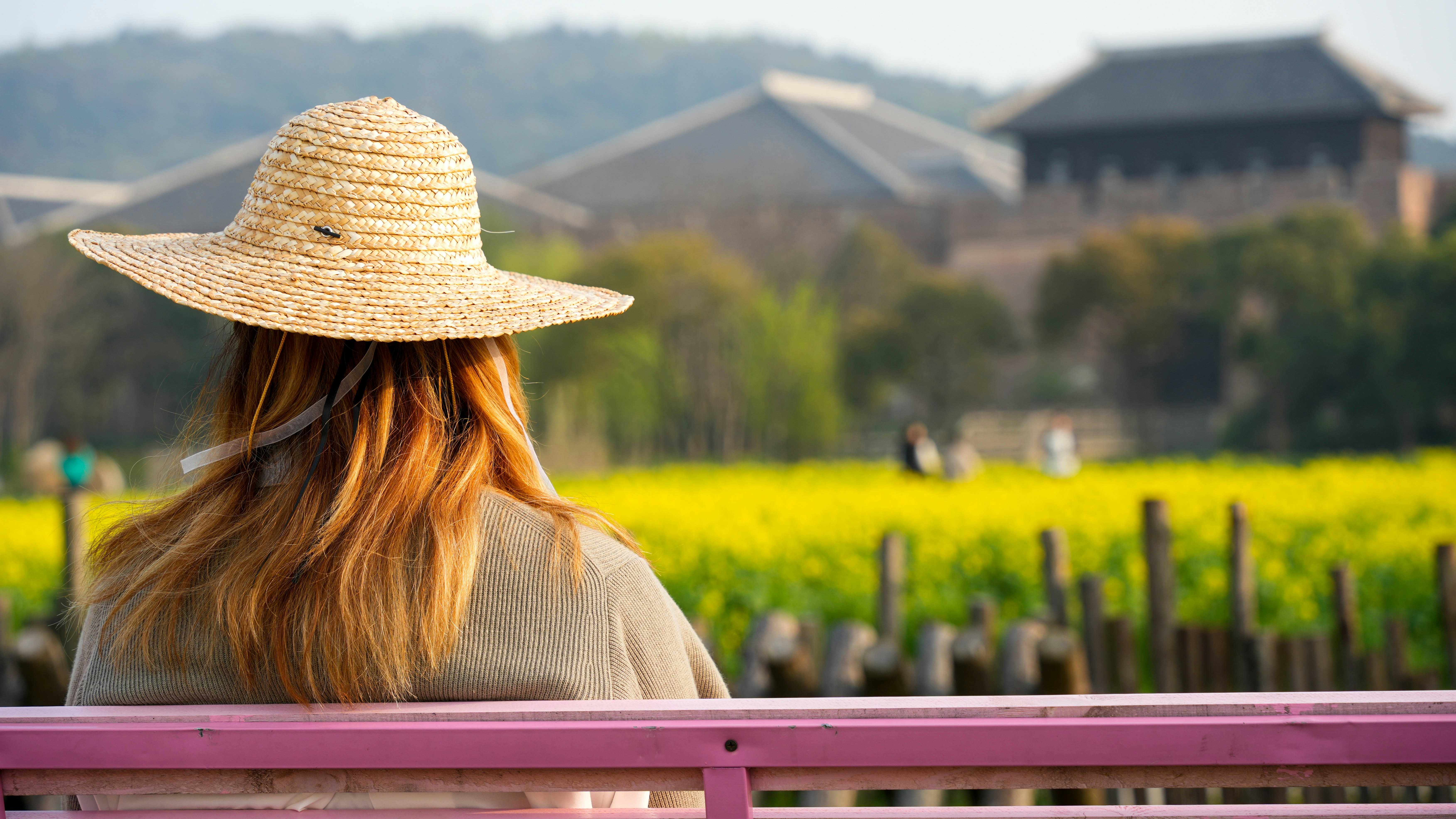 Woman in straw hat admiring a yellow flower field.