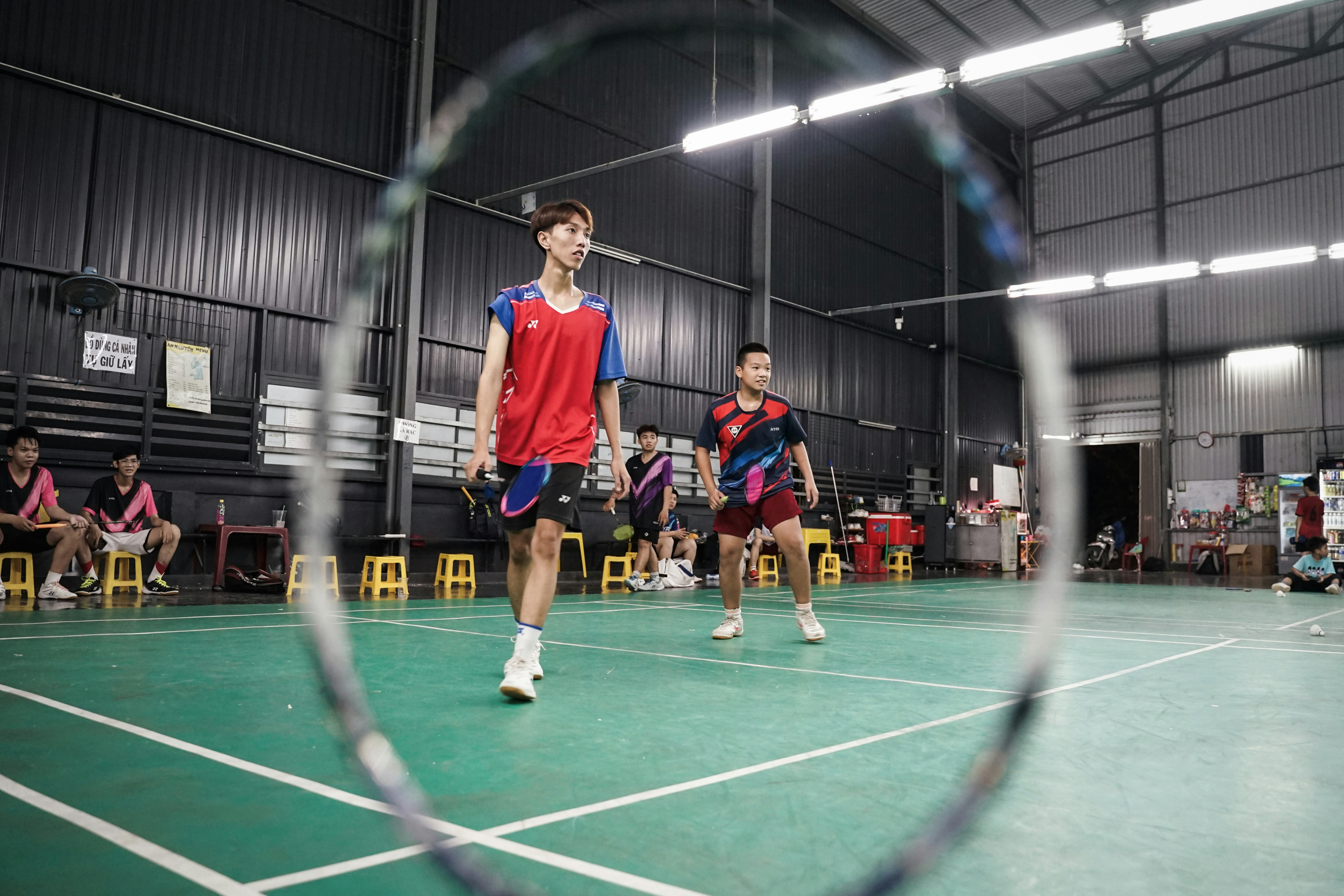 Badminton players on an indoor court through a racket.