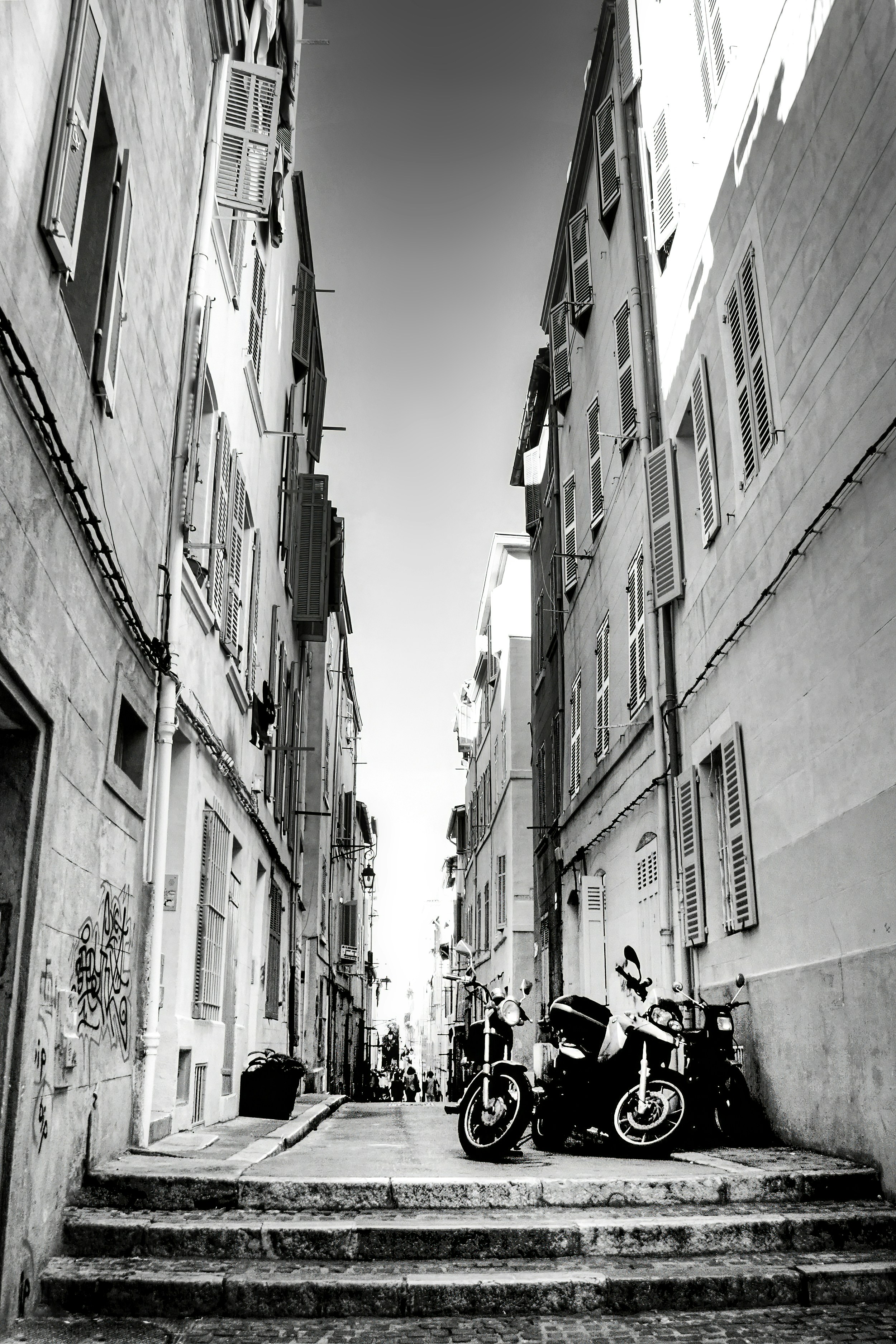 Black and white narrow street with buildings and parked motorcycles.