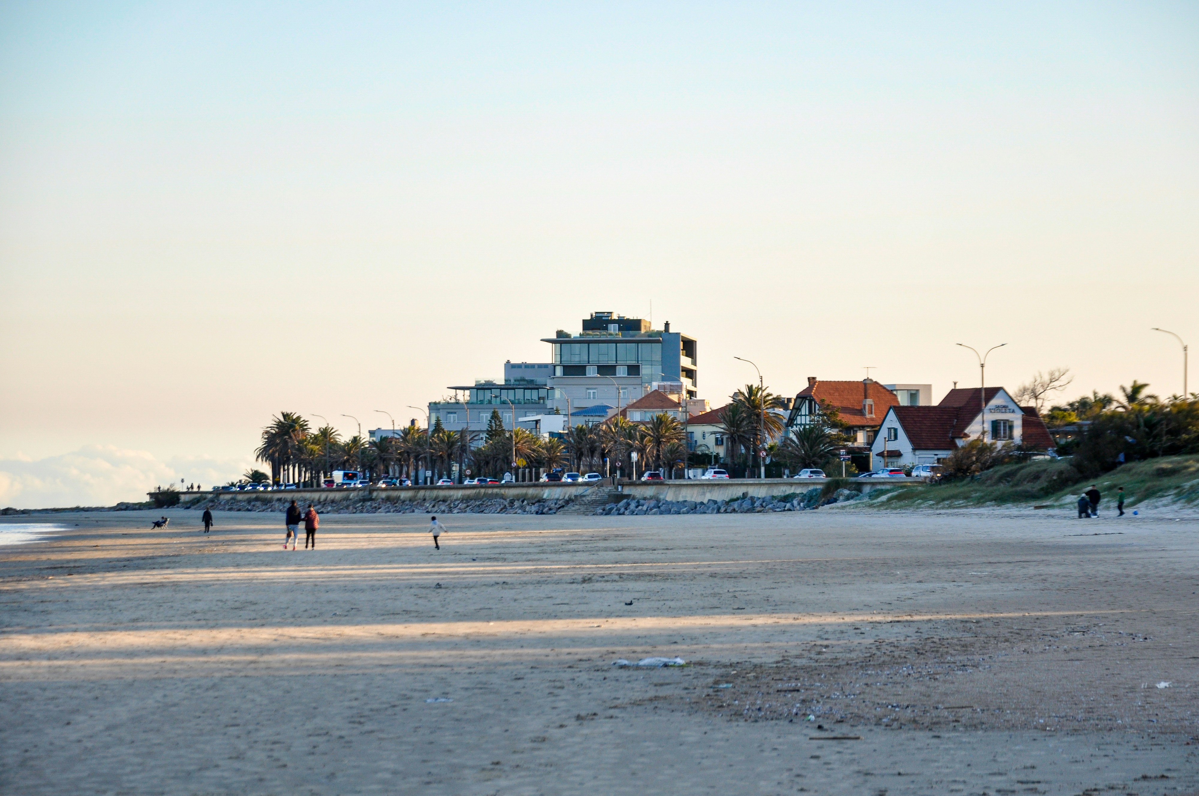 Sandy beach with distant buildings and people walking.