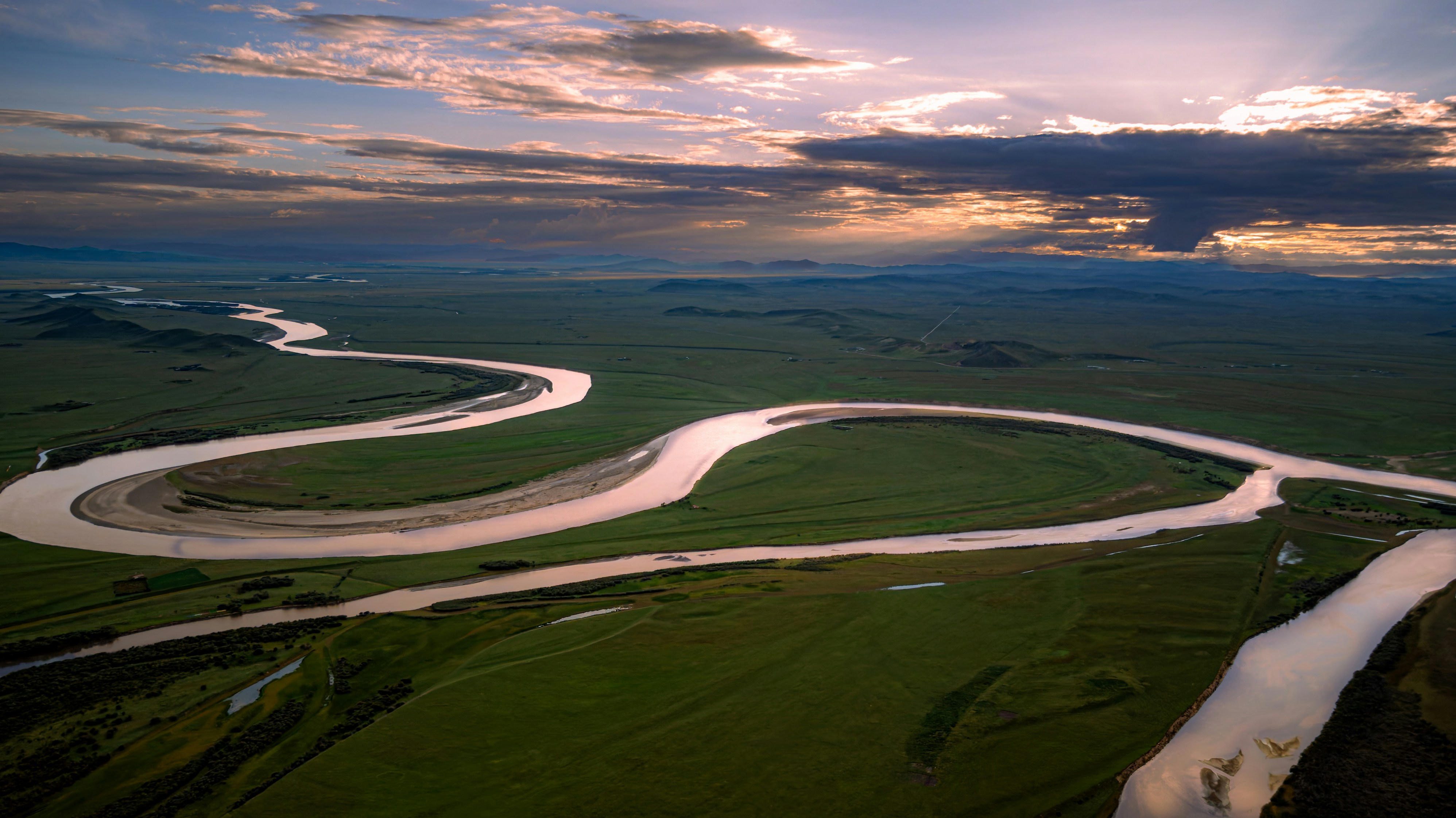 A winding river through green plains under a dramatic sunset.