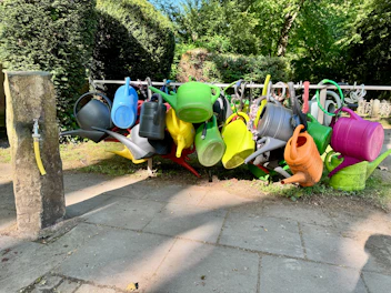 Colorful watering cans hanging on a bar near a faucet.