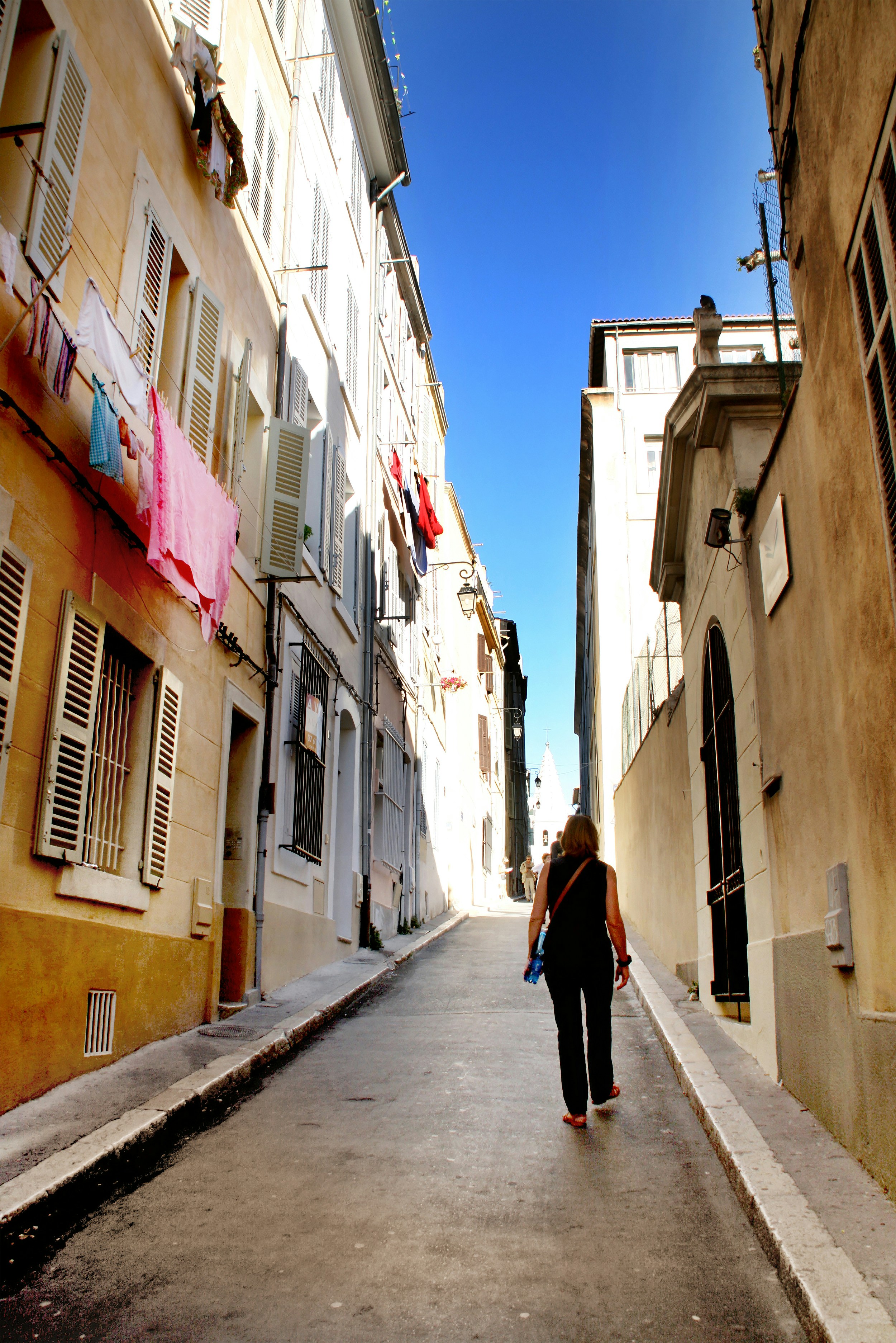 A person walks down a narrow street with laundry hanging.