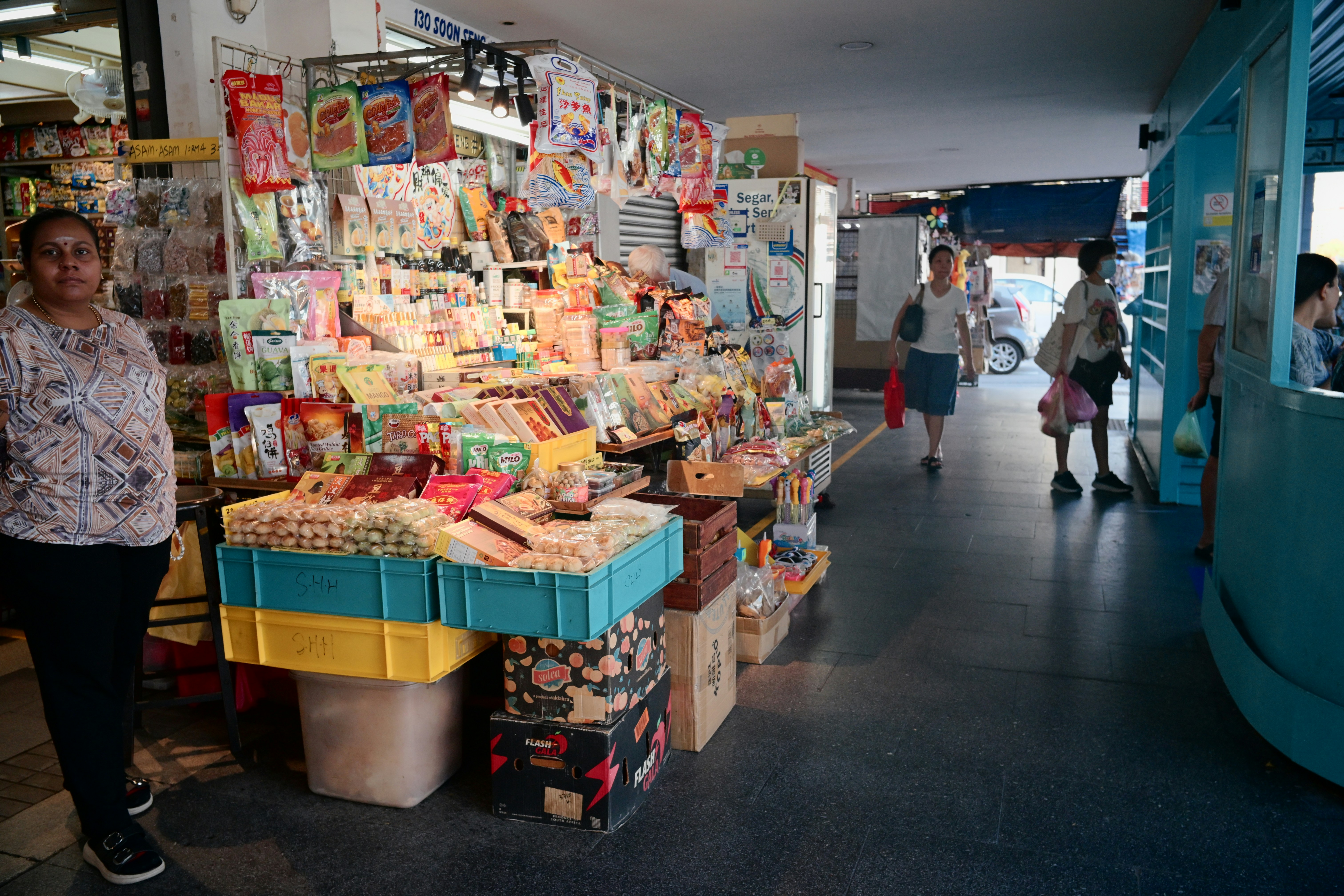 Woman stands by a crowded market stall with various goods.
