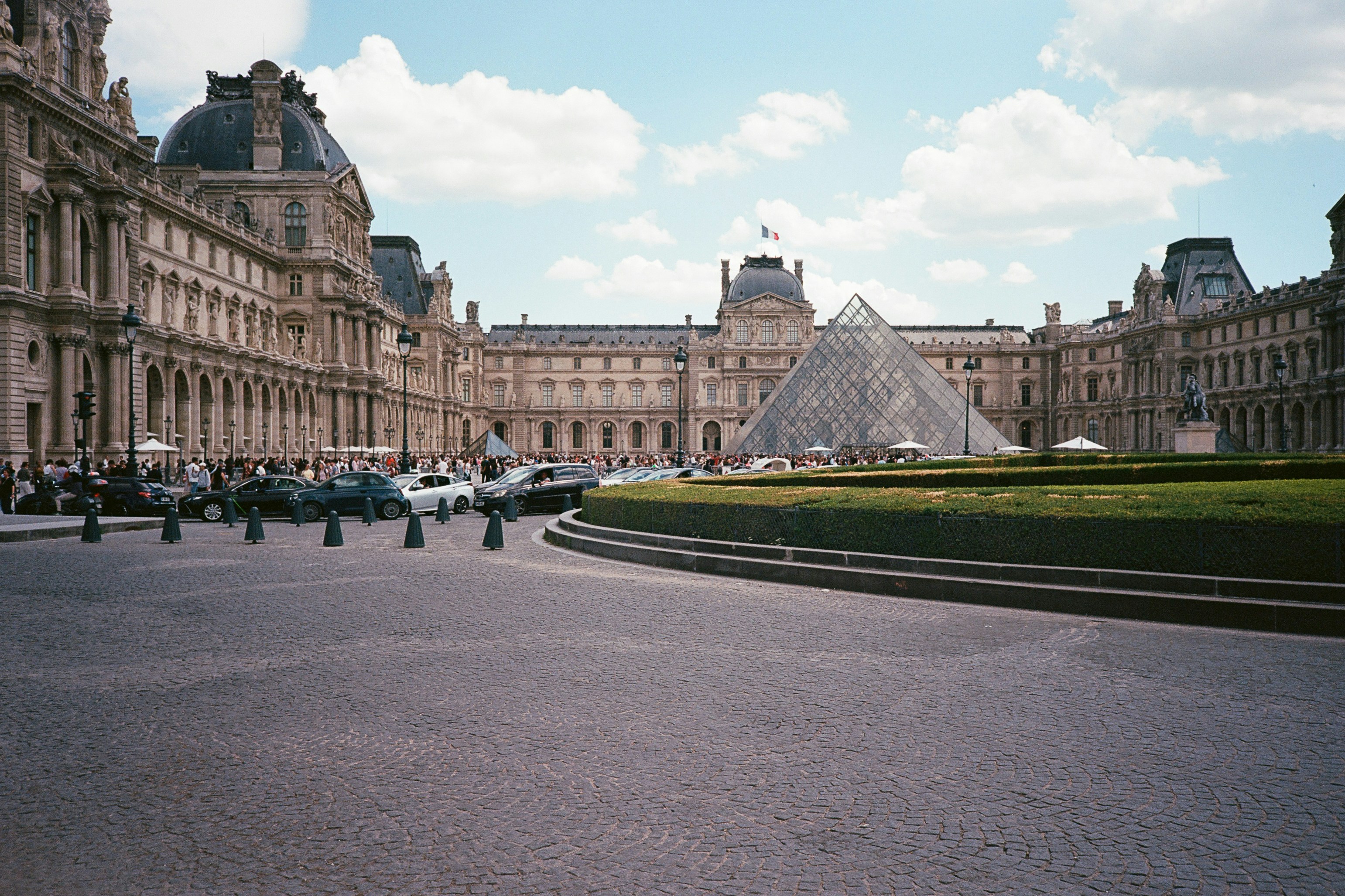Ikonisches Louvre-Museum mit Glaspyramide und grüner Landschaftsgestaltung.