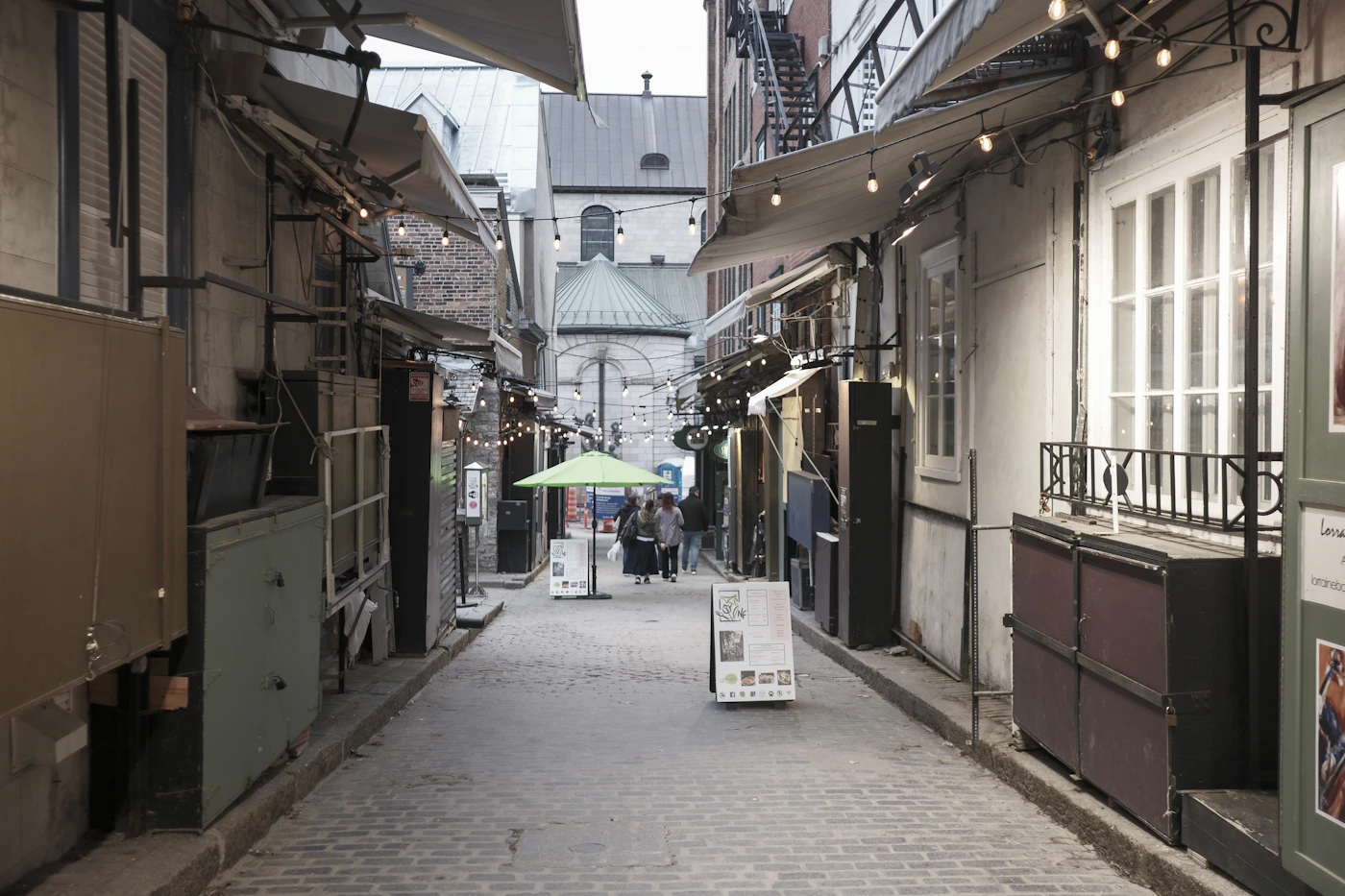 Narrow cobblestone alleyway in Old Quebec City lined with stone buildings and overhead string lights leading to a distant church at night