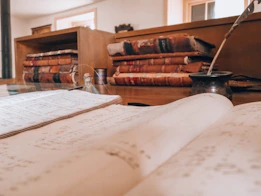 Open book, old books, and a quill on a desk