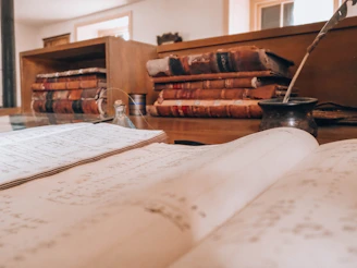 Open book, old books, and a quill on a desk
