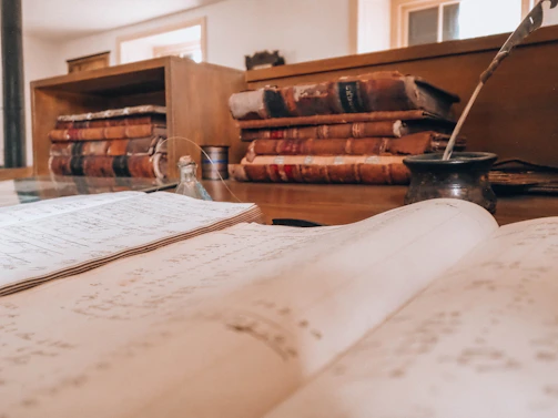 Open book, old books, and a quill on a desk
