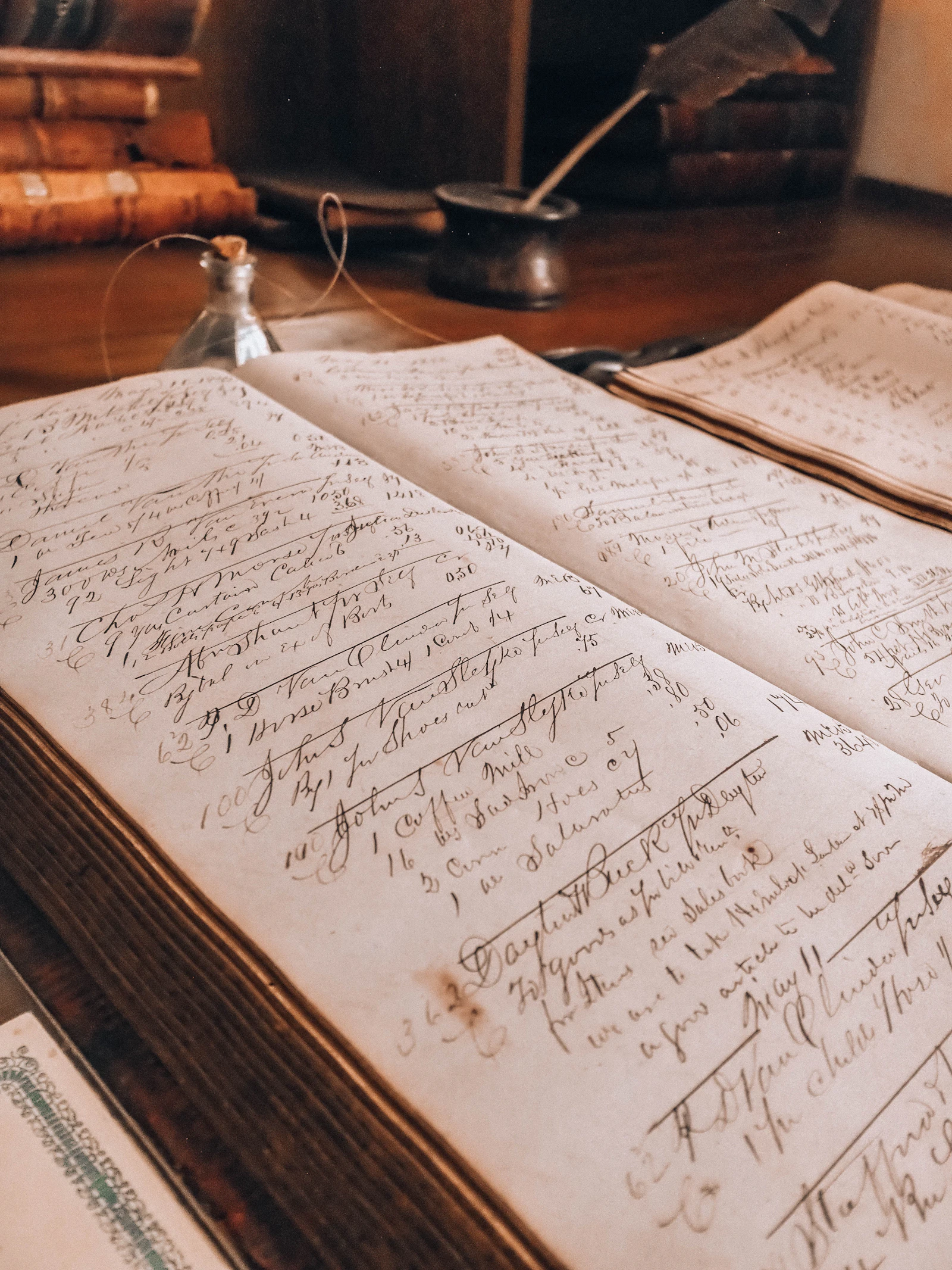 An open ledger of handwritten entries beside an inkwell and quill on a wooden desk