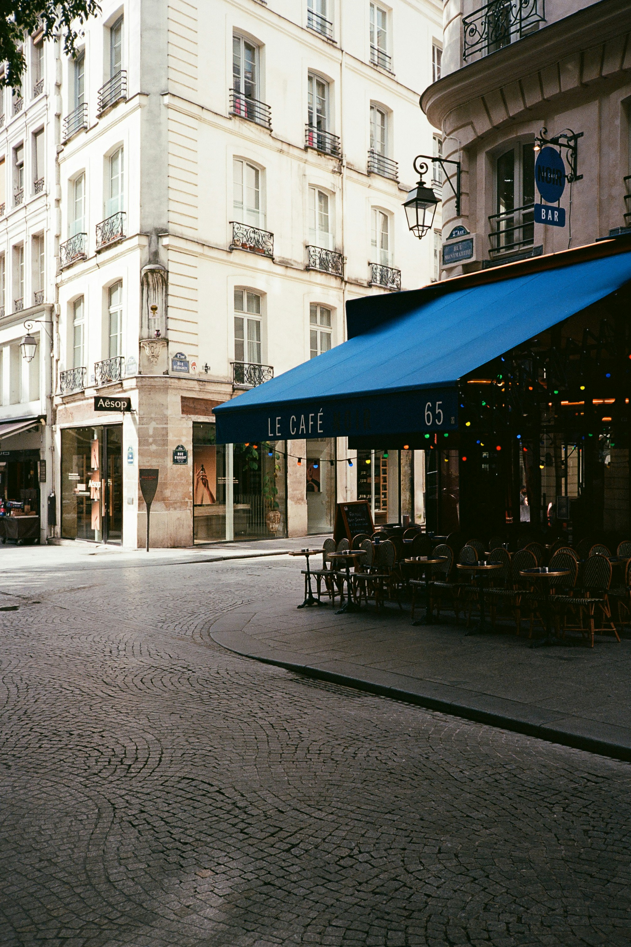 A cafe with a blue awning on a cobblestone street.