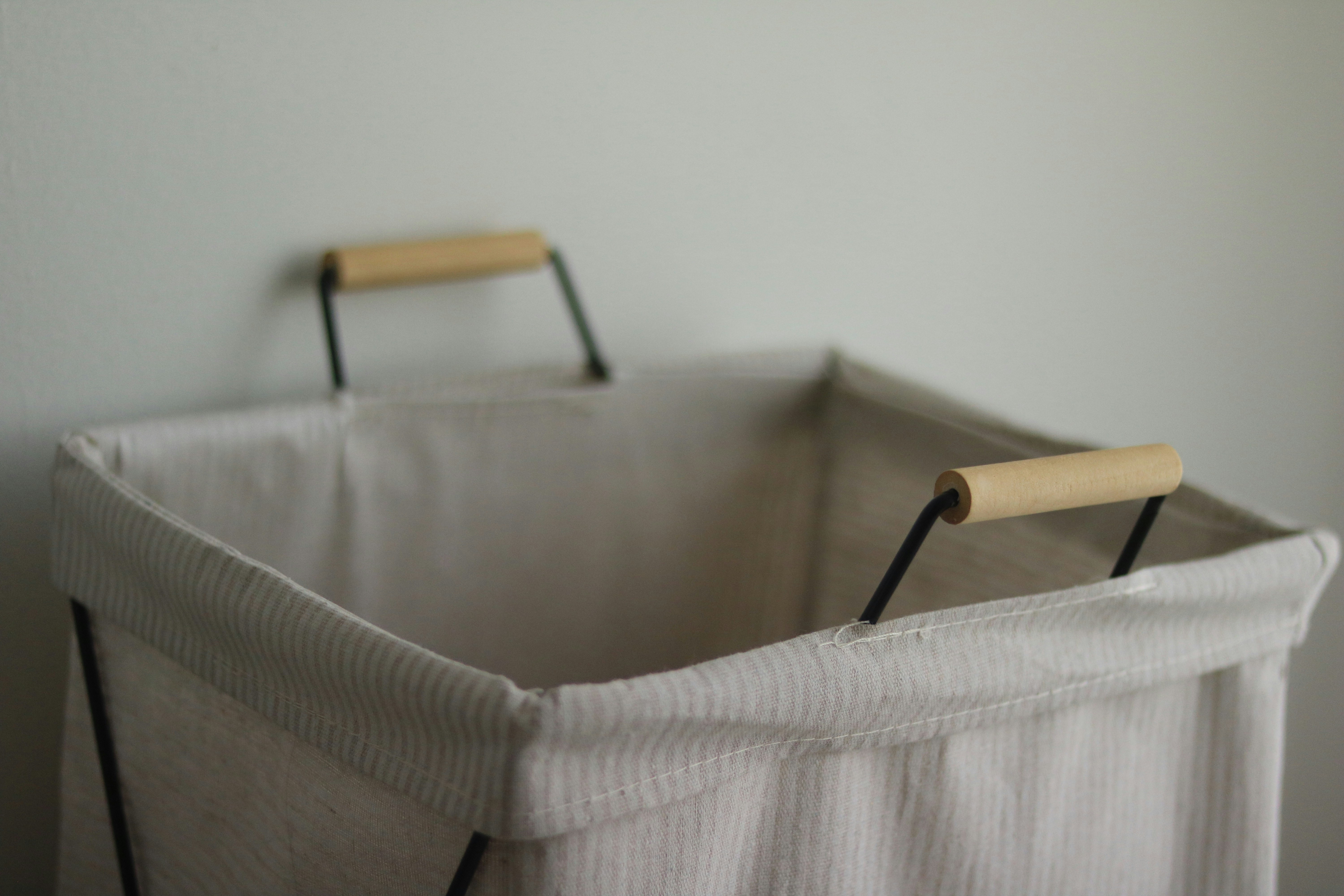 Un panier à linge vide, de couleur claire, avec des poignées en bois.