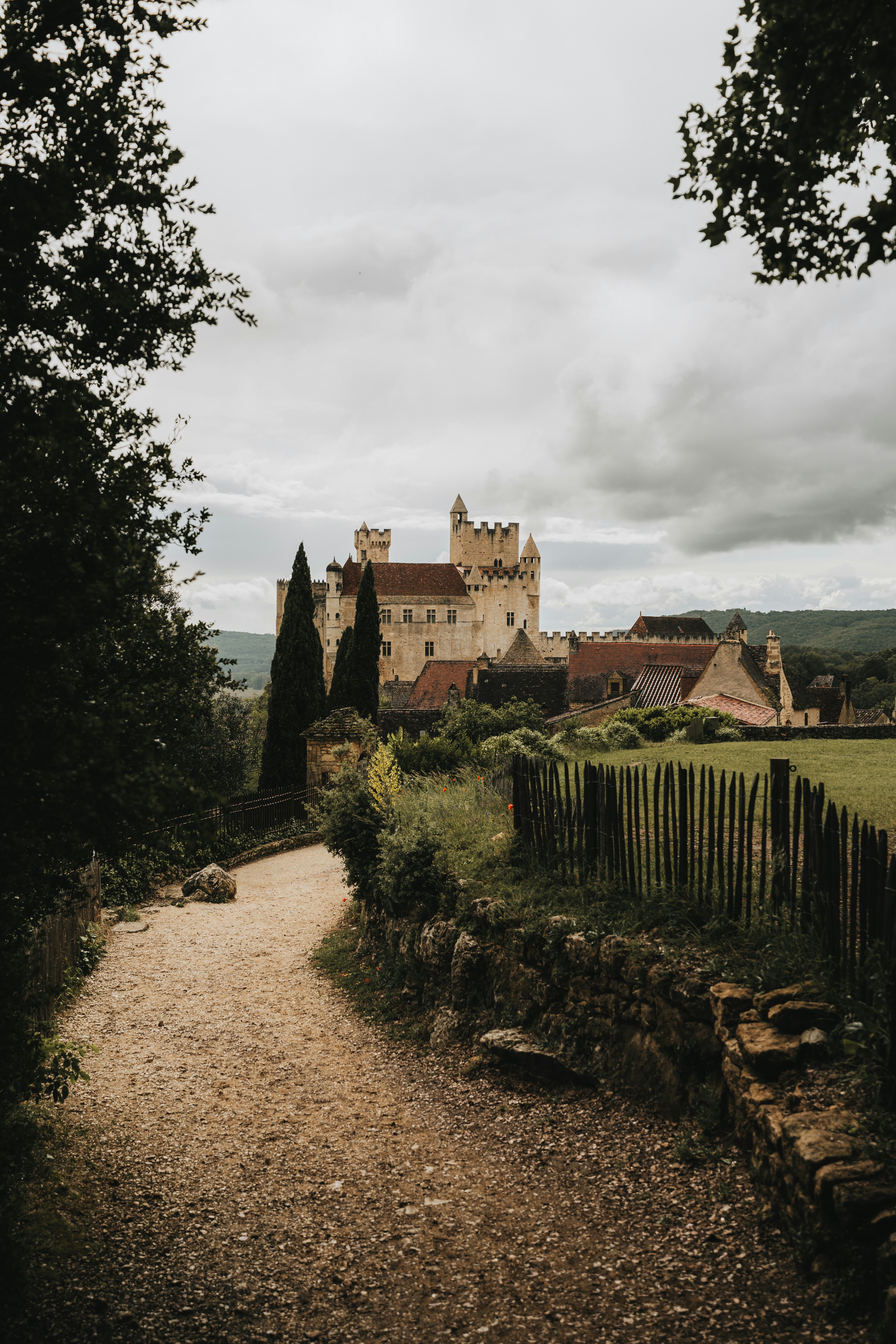 Winding path leads to a historic castle under cloudy sky.