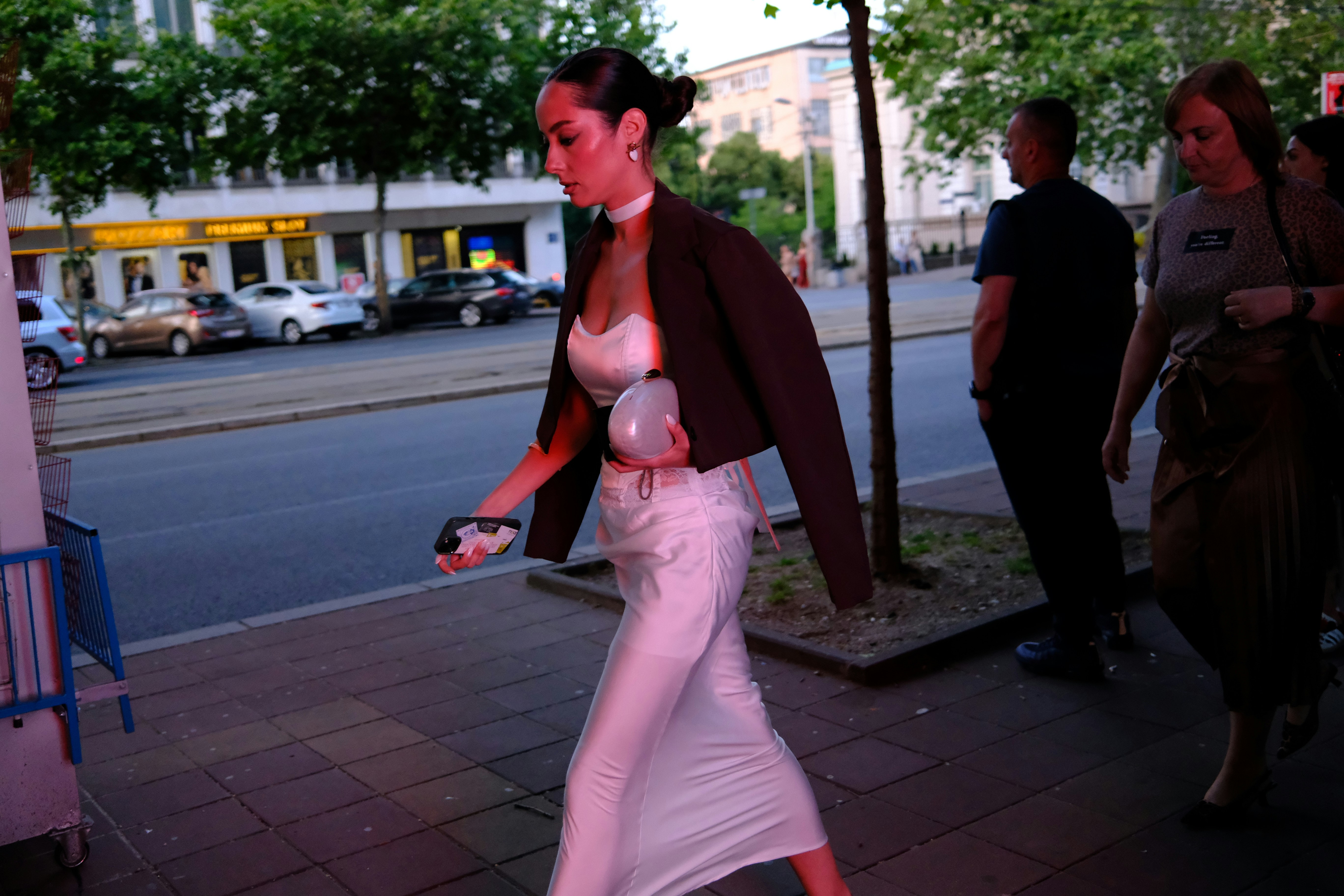 Elegant woman in white dress walking on a city street.