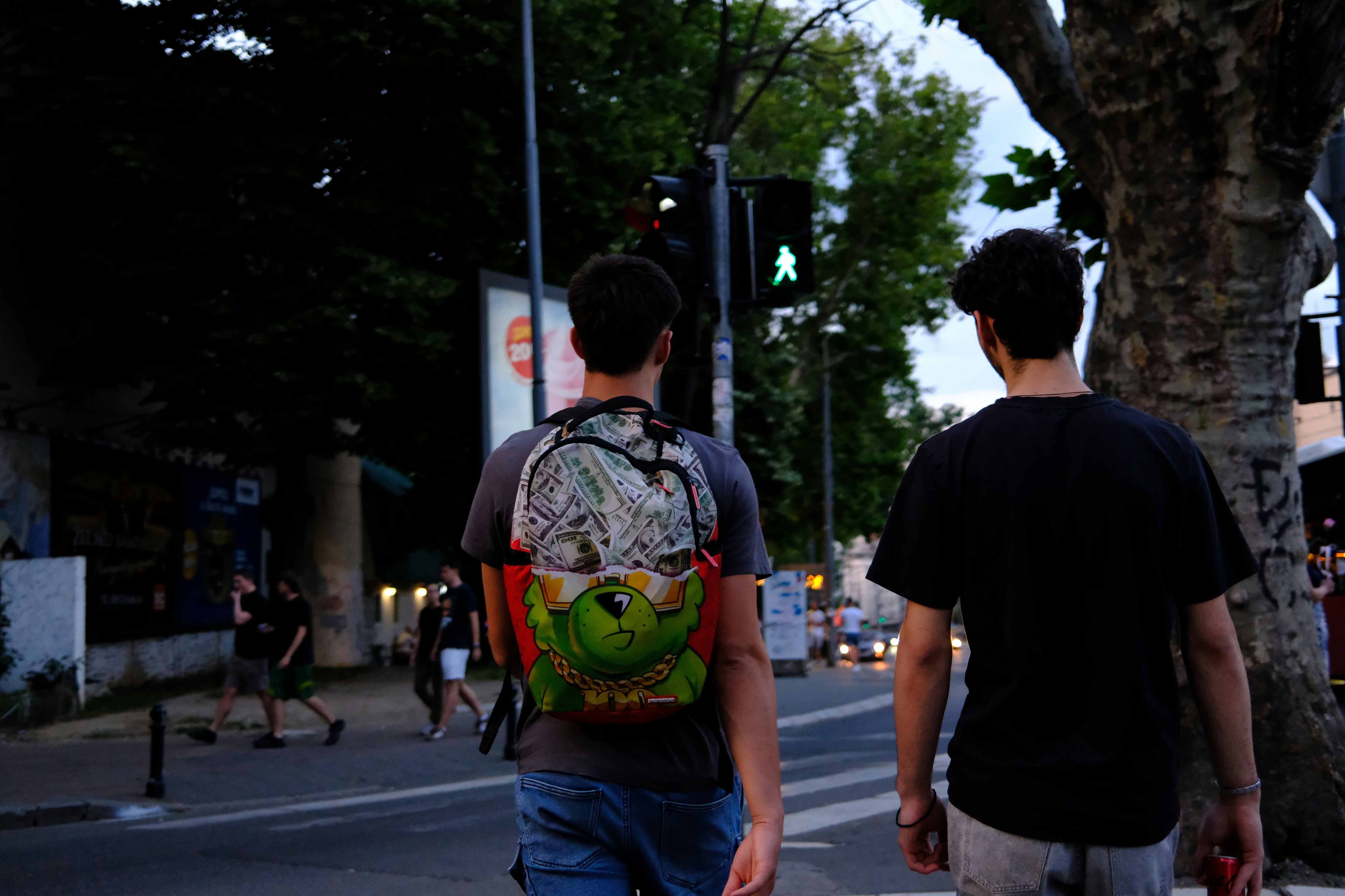 Two young men walk down a city street at dusk.