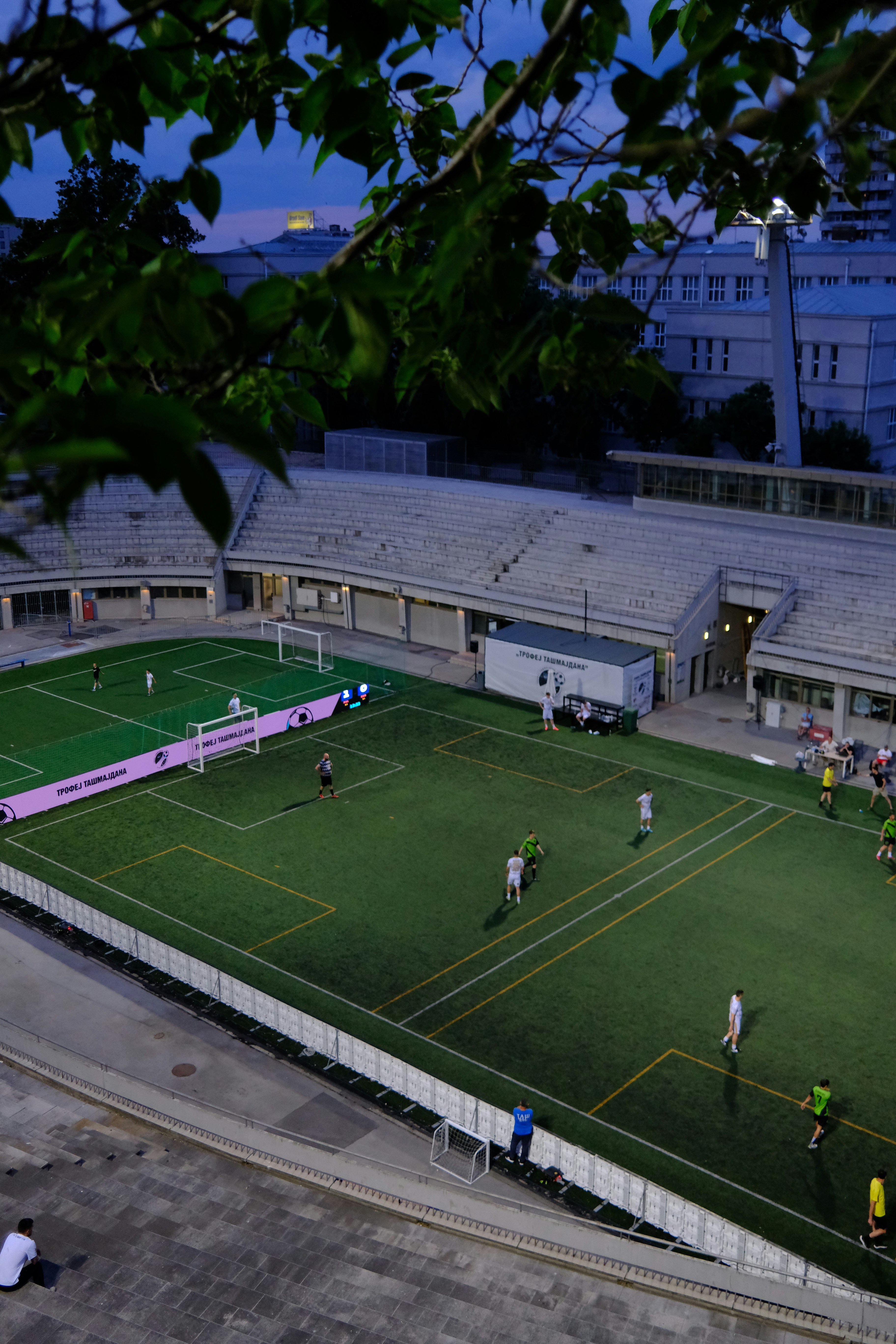 Pemain sepak bola di lapangan saat senja dengan tempat duduk stadion.