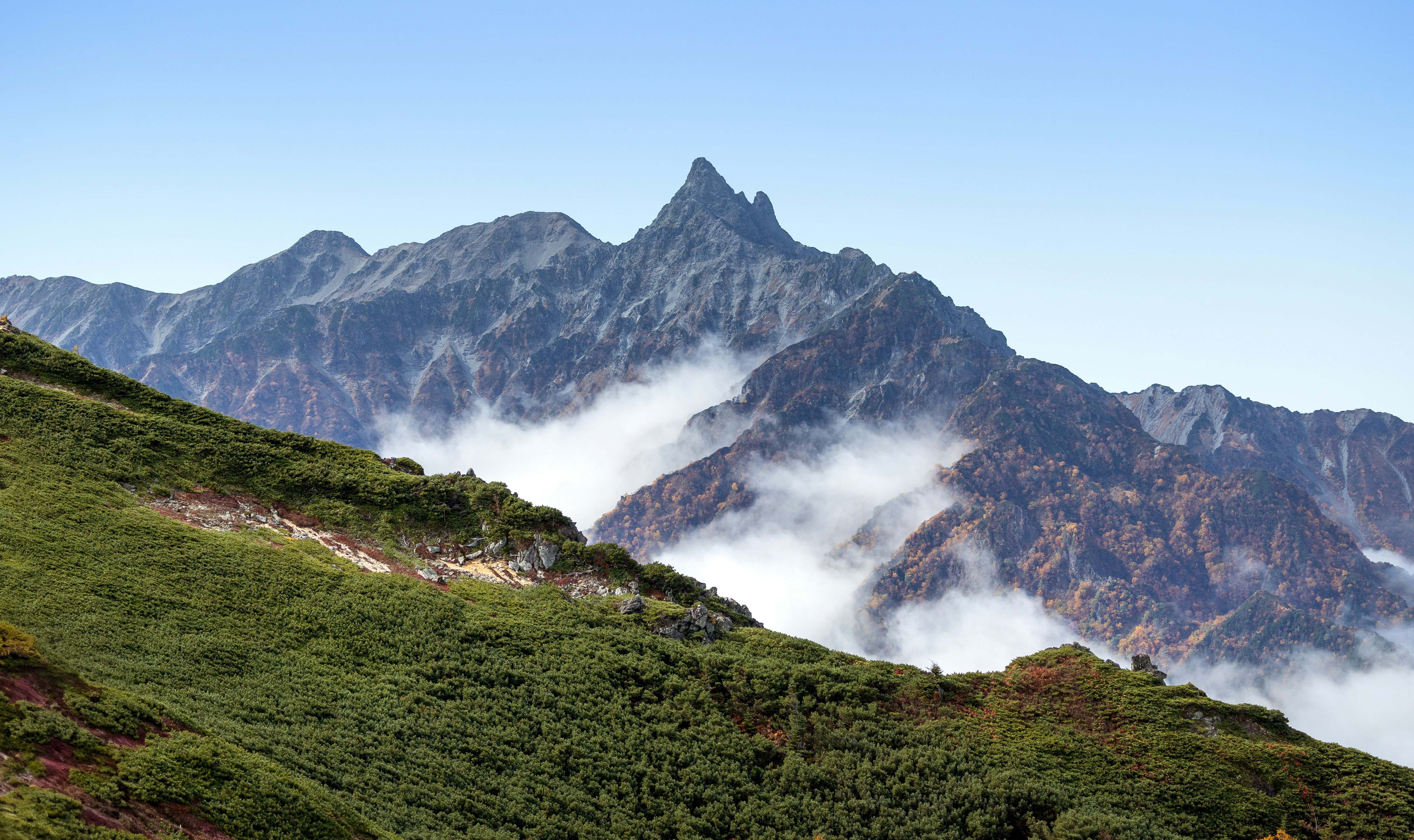 Green mountain slope leading to a rugged peak with clouds.