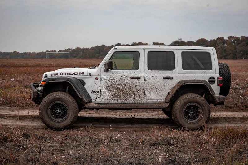 Dirty white Jeep with mud-splattered panels, grimy wheels, and road film covering the paint before detailing