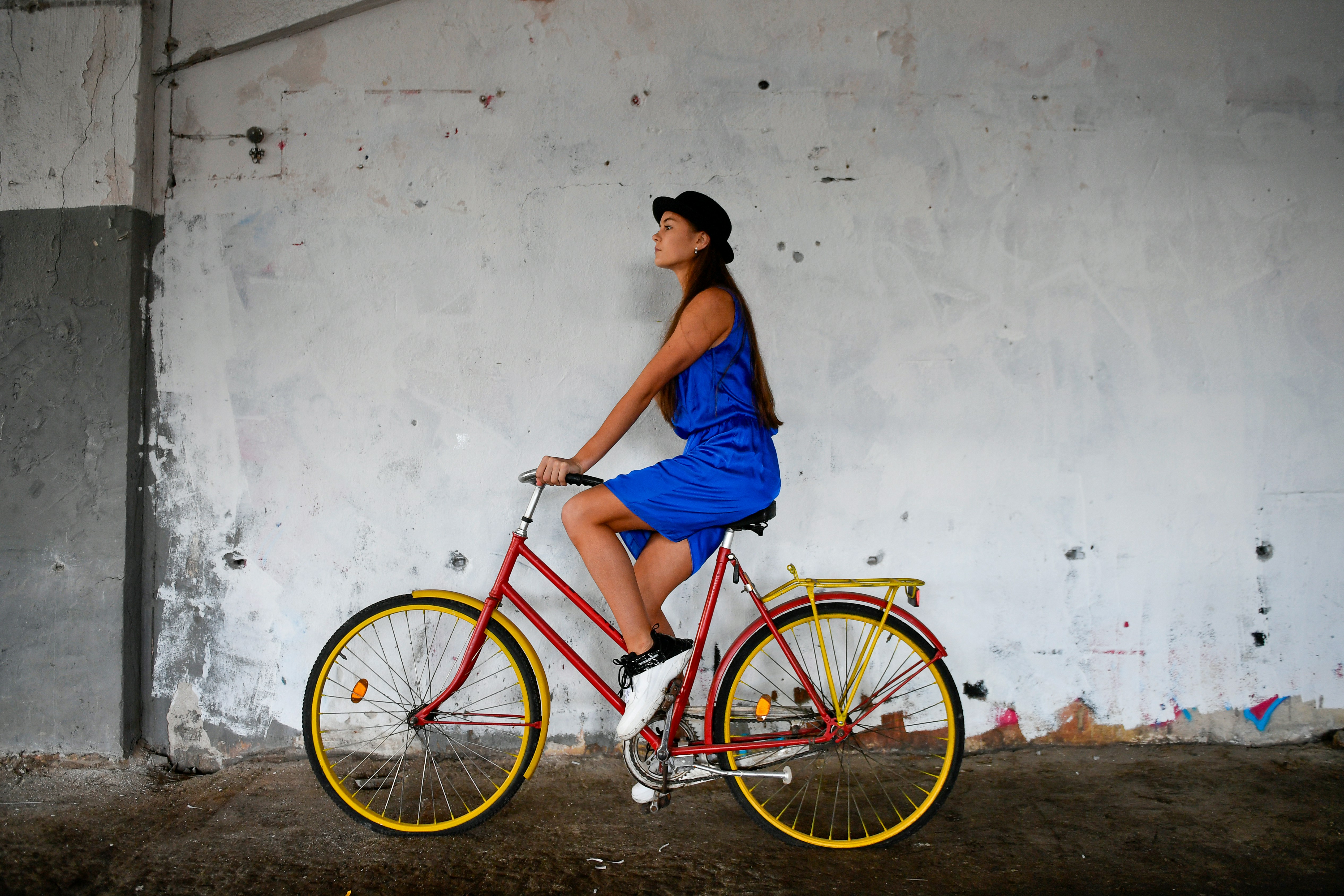 Woman in blue dress rides red bicycle with yellow rims.